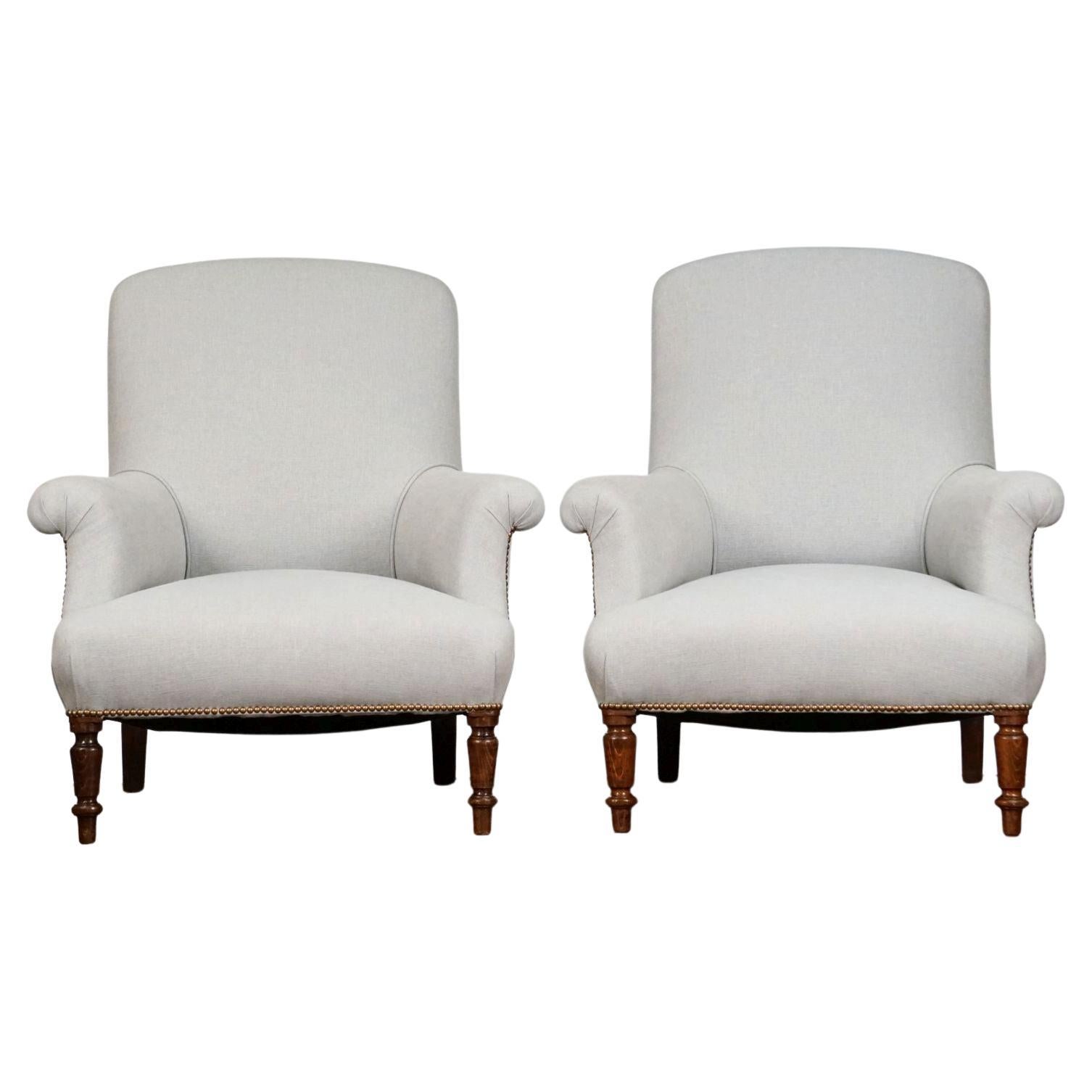 A fine pair of comfortable French upholstered armchairs, c.1880, completely refurbished and re-upholstered in a subtle grey pure linen fabric - in elegant contrast to the rich turned legs of brown walnut. Piped and trimmed with antiqued brass studs