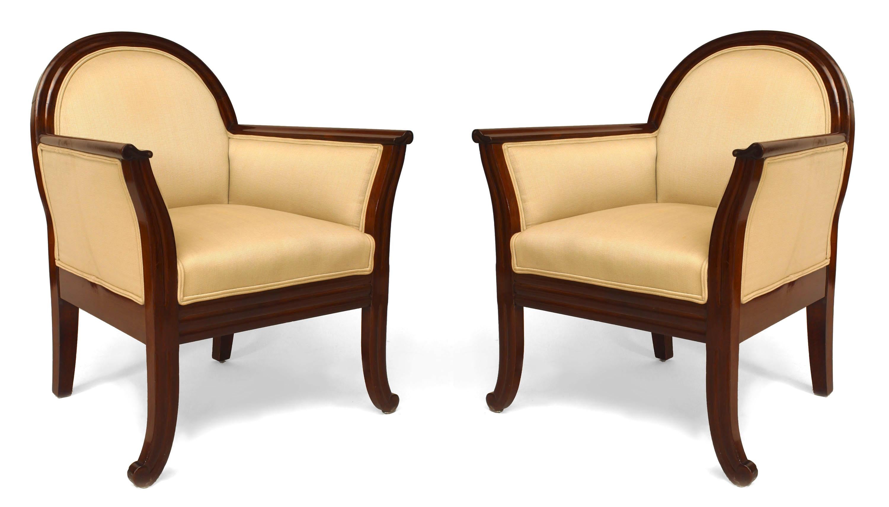 Pair of French Art Deco style mahogany club chairs with a rounded back and flared design front arms and legs with beige upholstery
