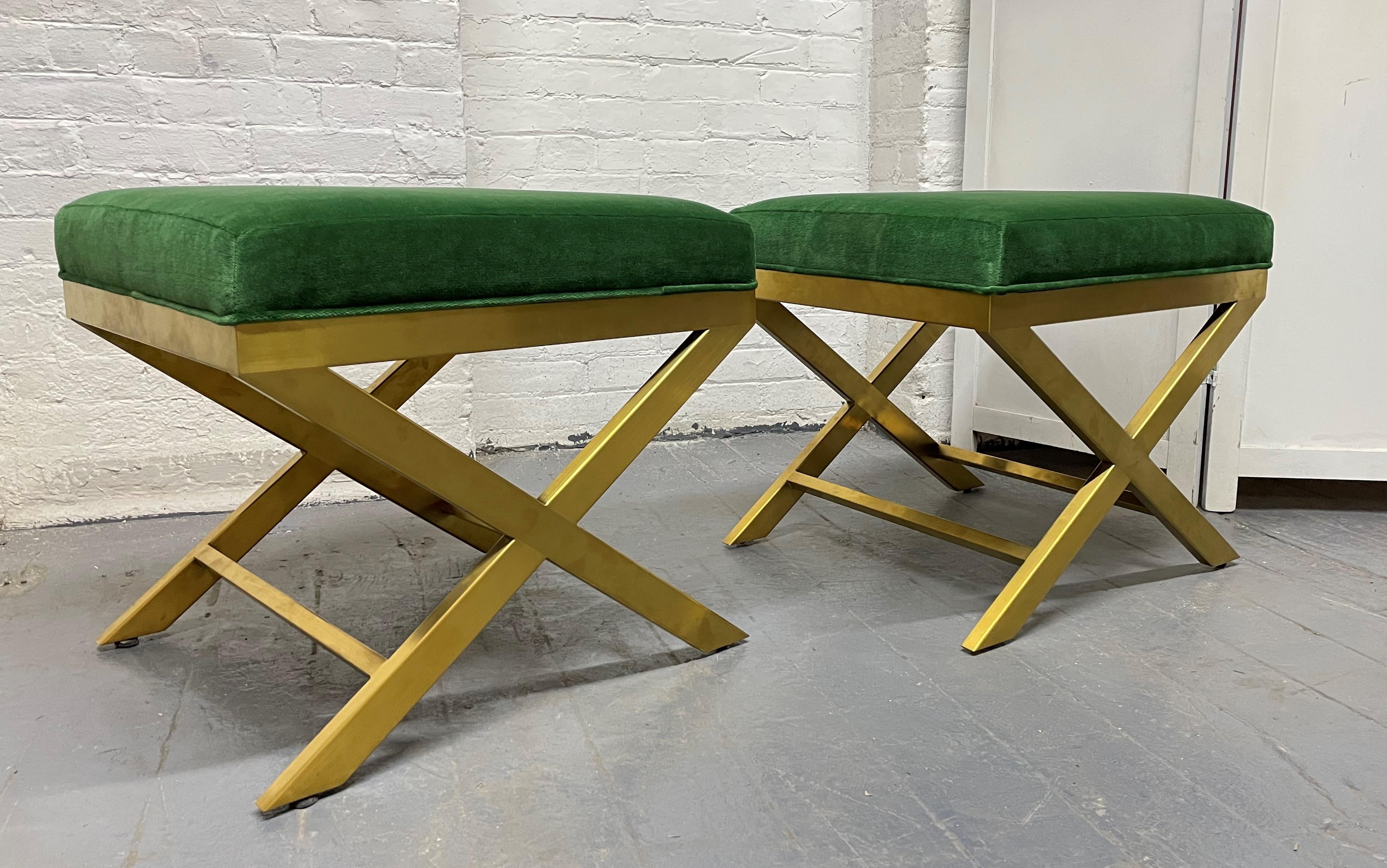 Pair of upholstered velvet and brass X-benches. The benches have brass frames and green velvet upholstery.
