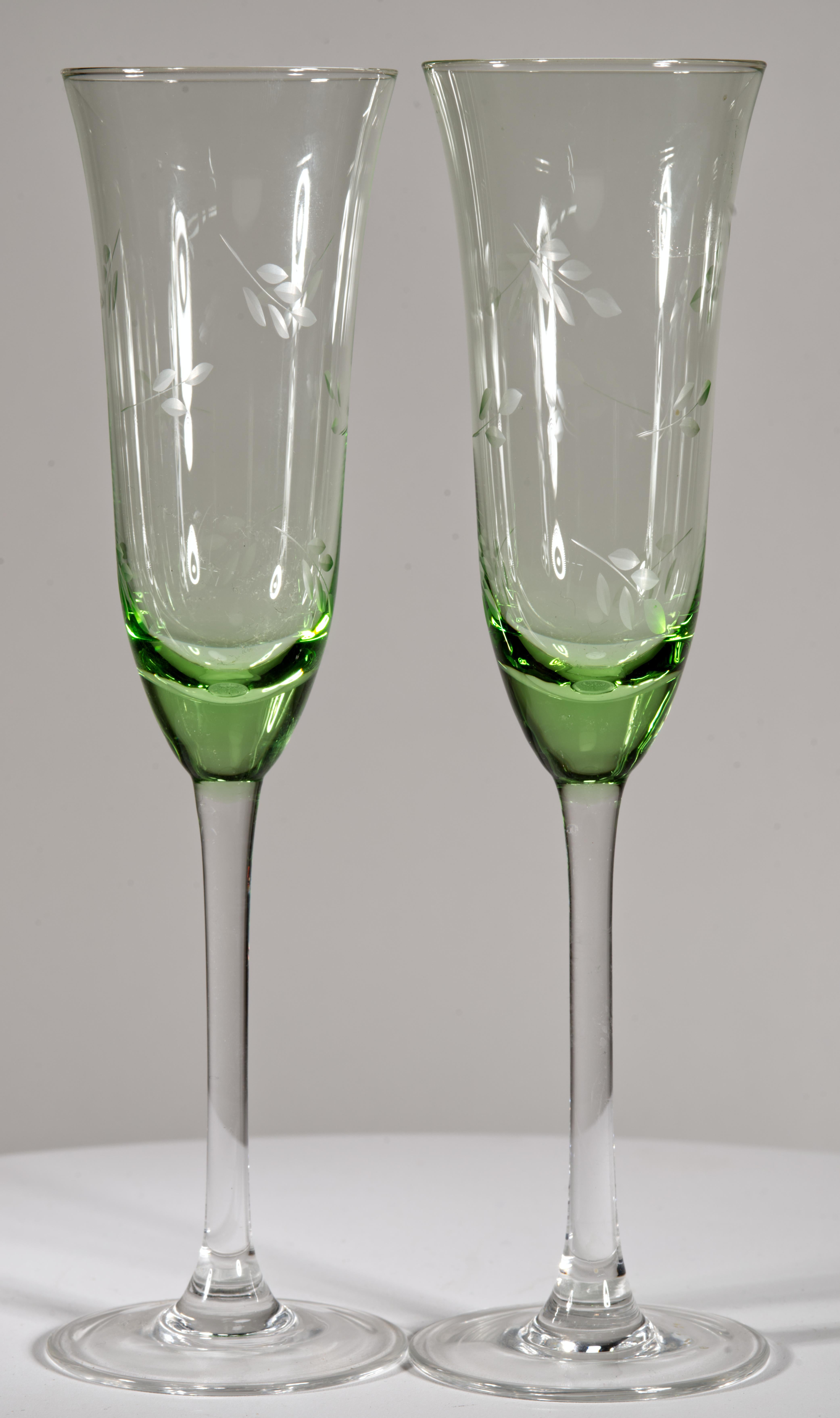 Vintage uranium green glass champagne flute glasses feature classic elongated shapes and minimal decor. The glasses are decorated with abstract etched flower decor; wide bases add stability while not distracting from ornate bowls, and balancing the