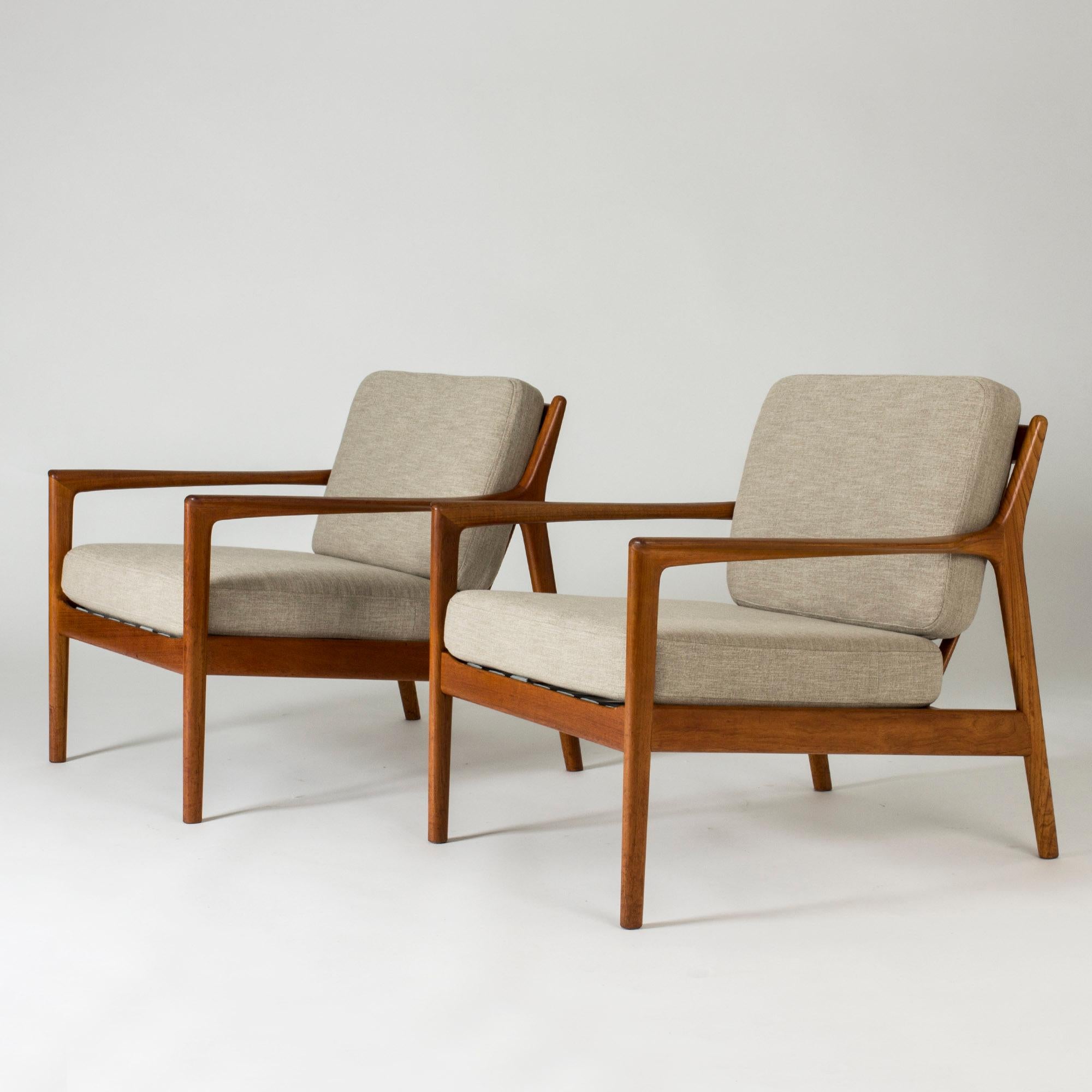 Pair of elegant and comfortable “USA 75” teak lounge chairs by Folke Ohlsson, with loose greige cushions. Beautifully sculpted armrests and ribbing in the back.