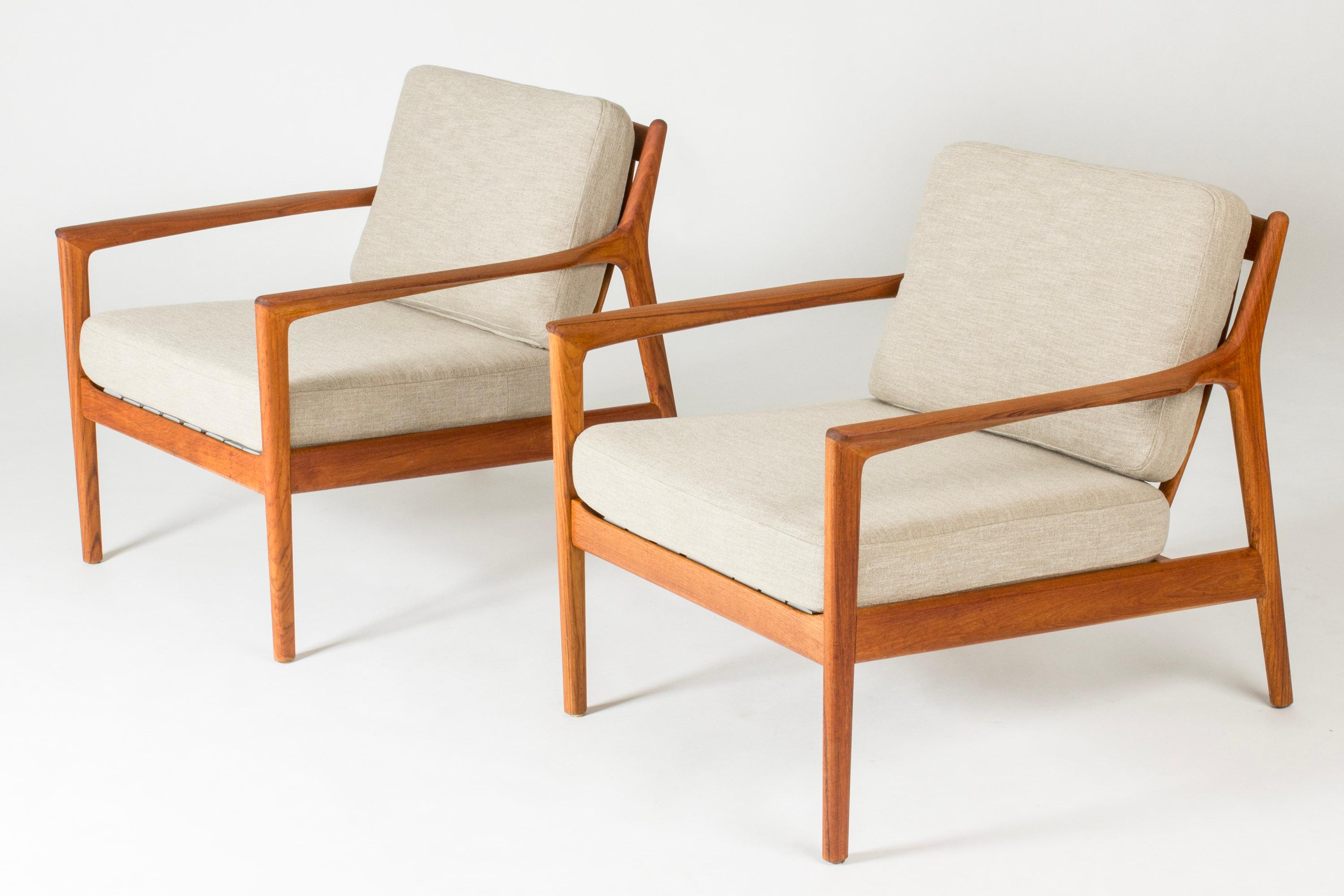 Pair of elegant and comfortable “USA 75” teak lounge chairs by Folke Ohlsson, with loose greige cushions. Beautifully sculpted armrests and ribbing in the back.