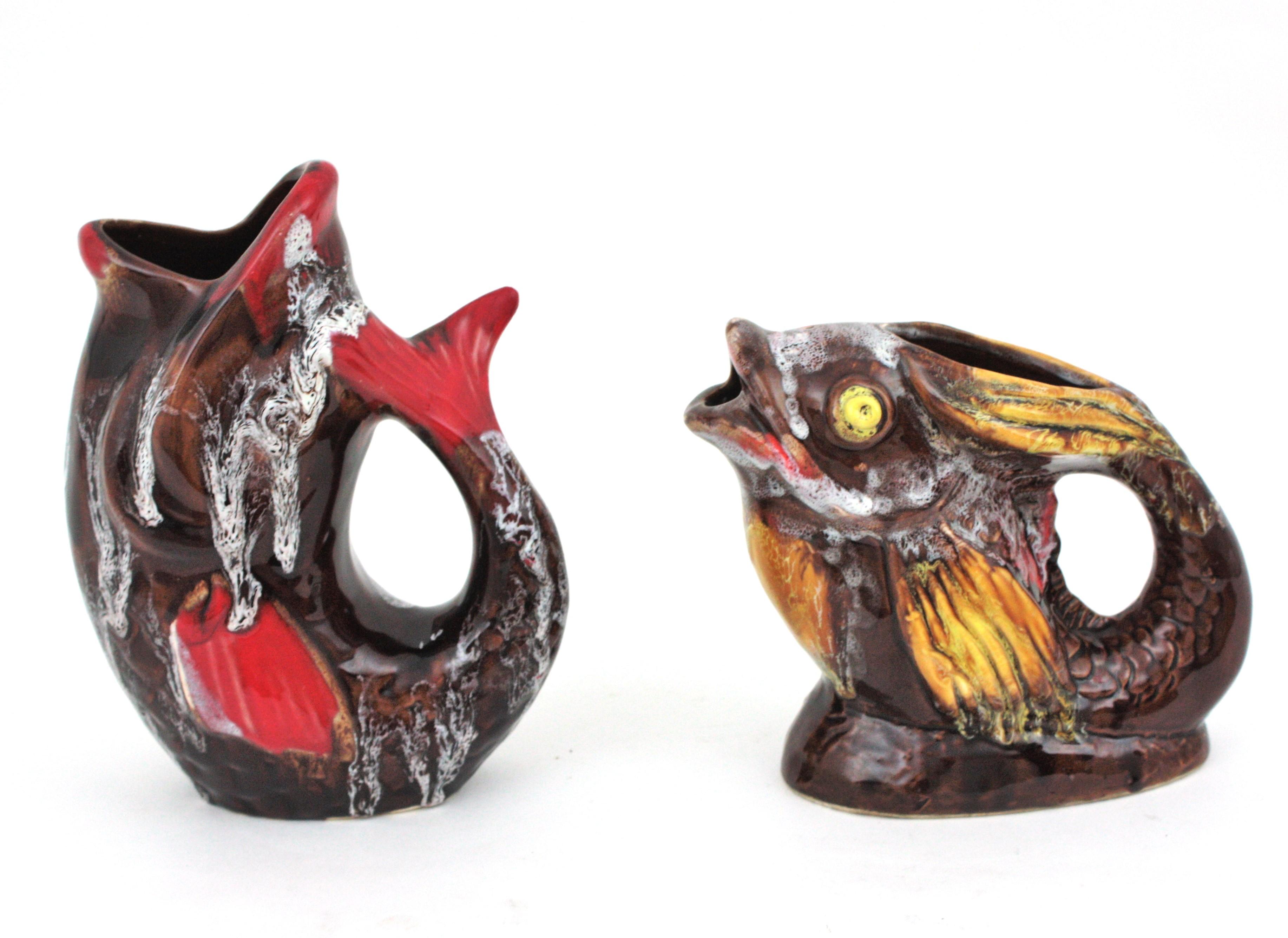 Unmatching pair of Modernist glazed ceramic gurgling fish water jugs / pitchers by Vallauris, France, 1950s-1960s
Eye-catching hand painted fat lava gurgle fish vases in brown glazed ceramic with yellow, white and red accents. 
The large fish glug