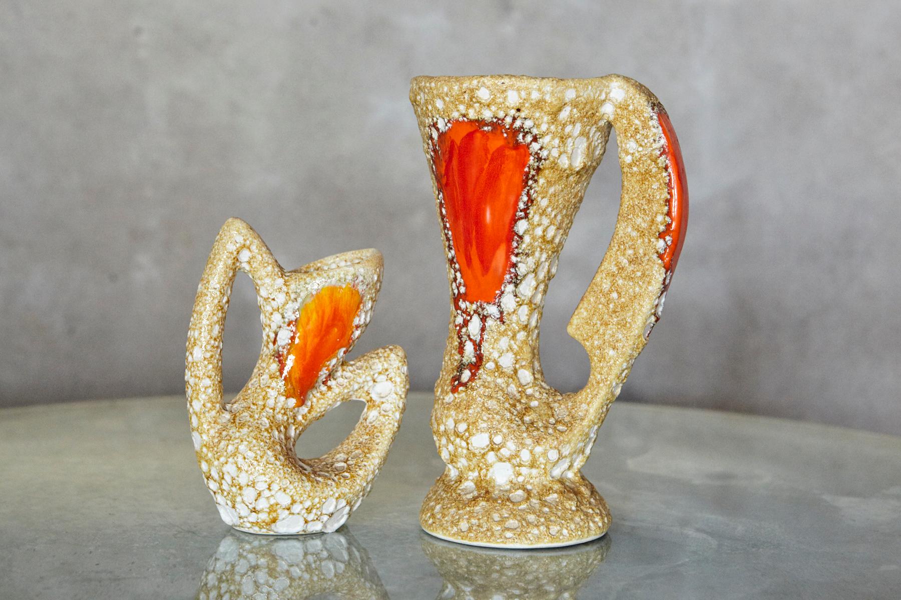 Coppia di vasi scultorei in ceramica in stile Vallauris, probabilmente risalenti alla metà del XX secolo. Ogni vaso ha un corpo allungato e affusolato con una maniglia integrata e un piede circolare, creando una silhouette aperta e grafica.
La