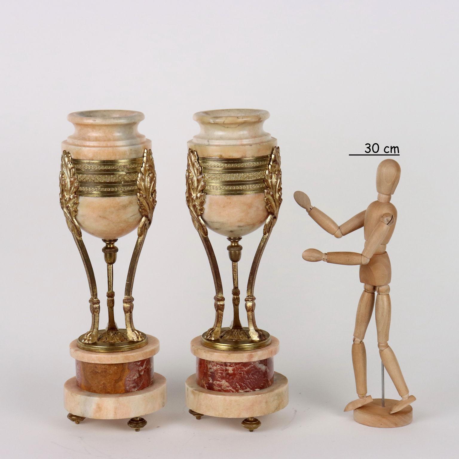 Pair of vases in pink marble and gilt bronze. A tripod vase with feral paw feet rests on a circular marble base and the top marble cup is held by three flames with a gilded and chiseled bronze band.