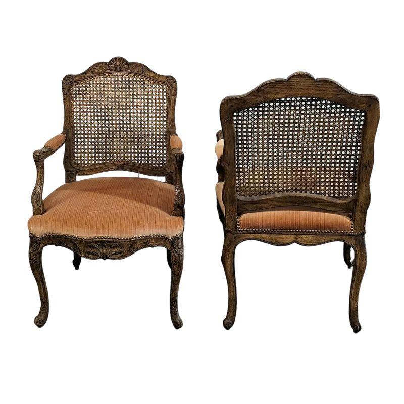 A vintage pair of velvet upholstered French style cane back armchairs. The Louis XV style fauteuils pair have carved frames and cabriole legs with a shell motif to the back and carved details on the chair arms and apron. Seats and arm rests are
