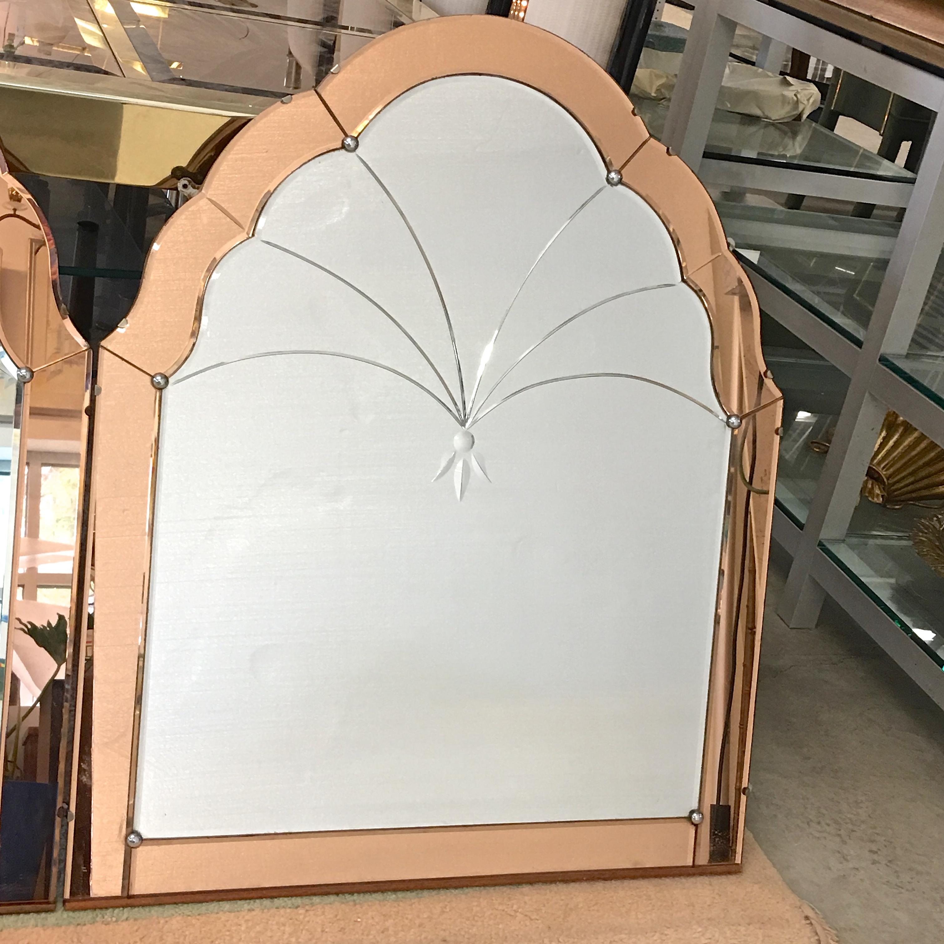 
Pair of 1930's Venetian wall mirrors of arched form with scalloped edges, having bevel cut design to the central mirror with apricot peach colored mirrored glass surrounds. Finished with a panel board back. 

Price is for the pair.
