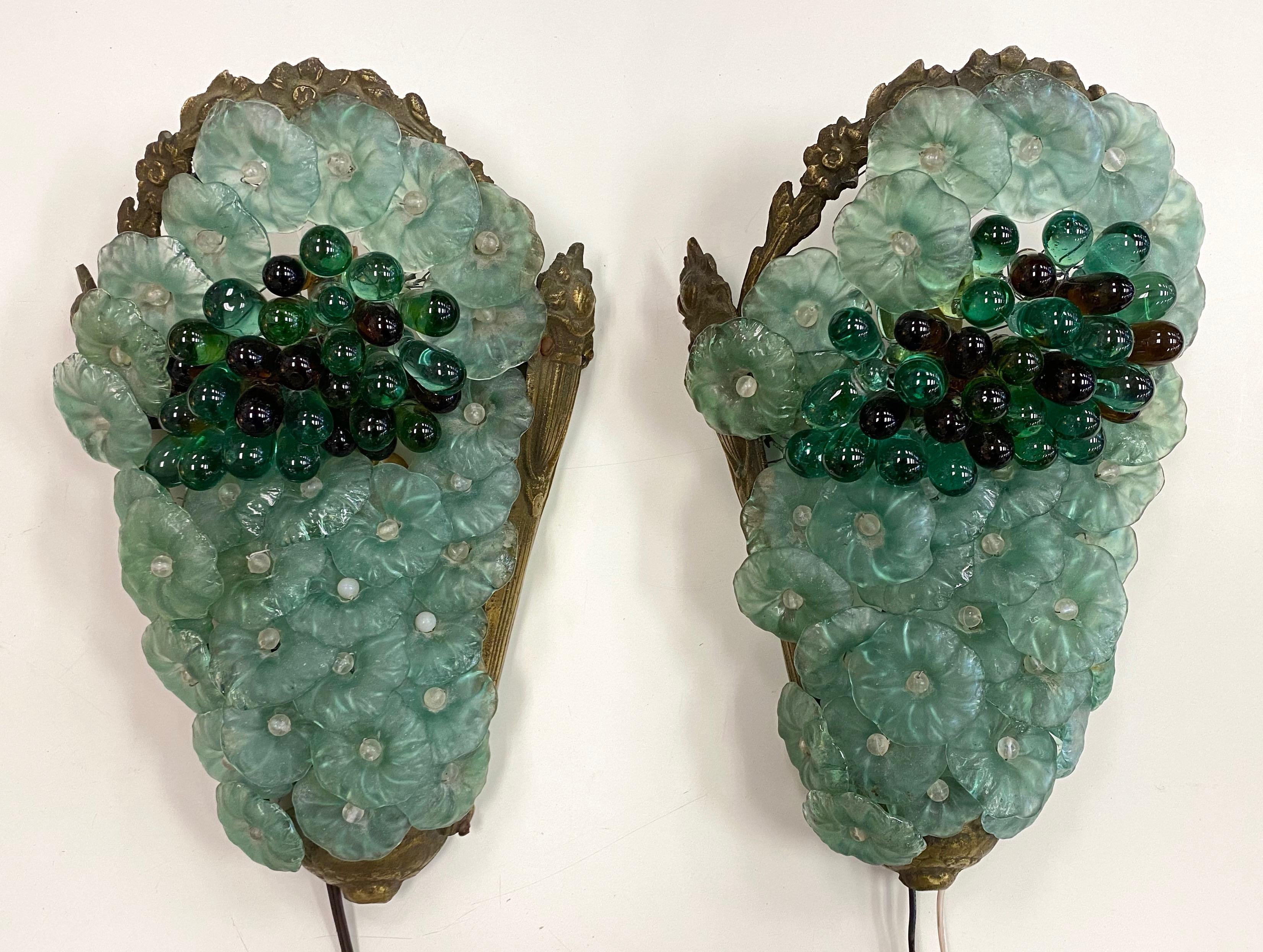 A beautiful pair of 1950s brass and Venetian or Murano glass floral and grape cluster lighted wall sconces.

Tight grouping of richly hued emerald green and dark amber glass grapes nestled within a dense field of overlapping mint greenish-blue