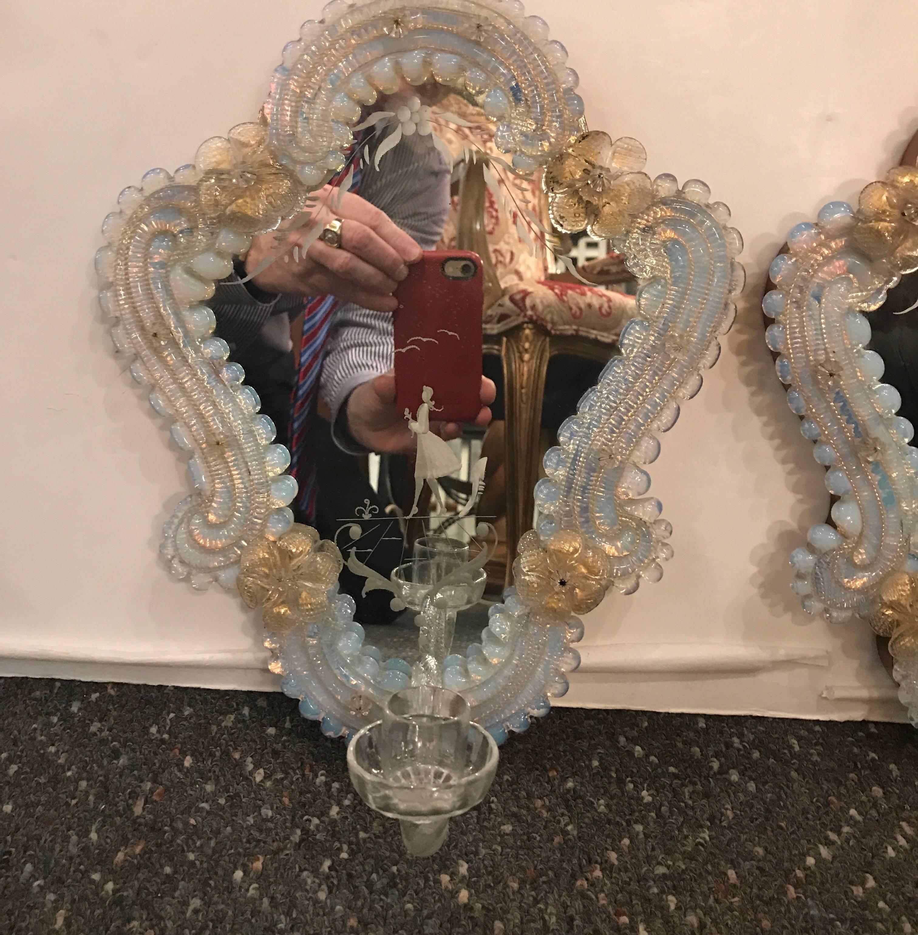 Opulent handblown Venetian glass sconces with opaline frames and gold fleck flowers. The mirrored backs with an etched design with an arm in handblown glass with a candle cup. The back of the shield is solid walnut. These sconces are original and