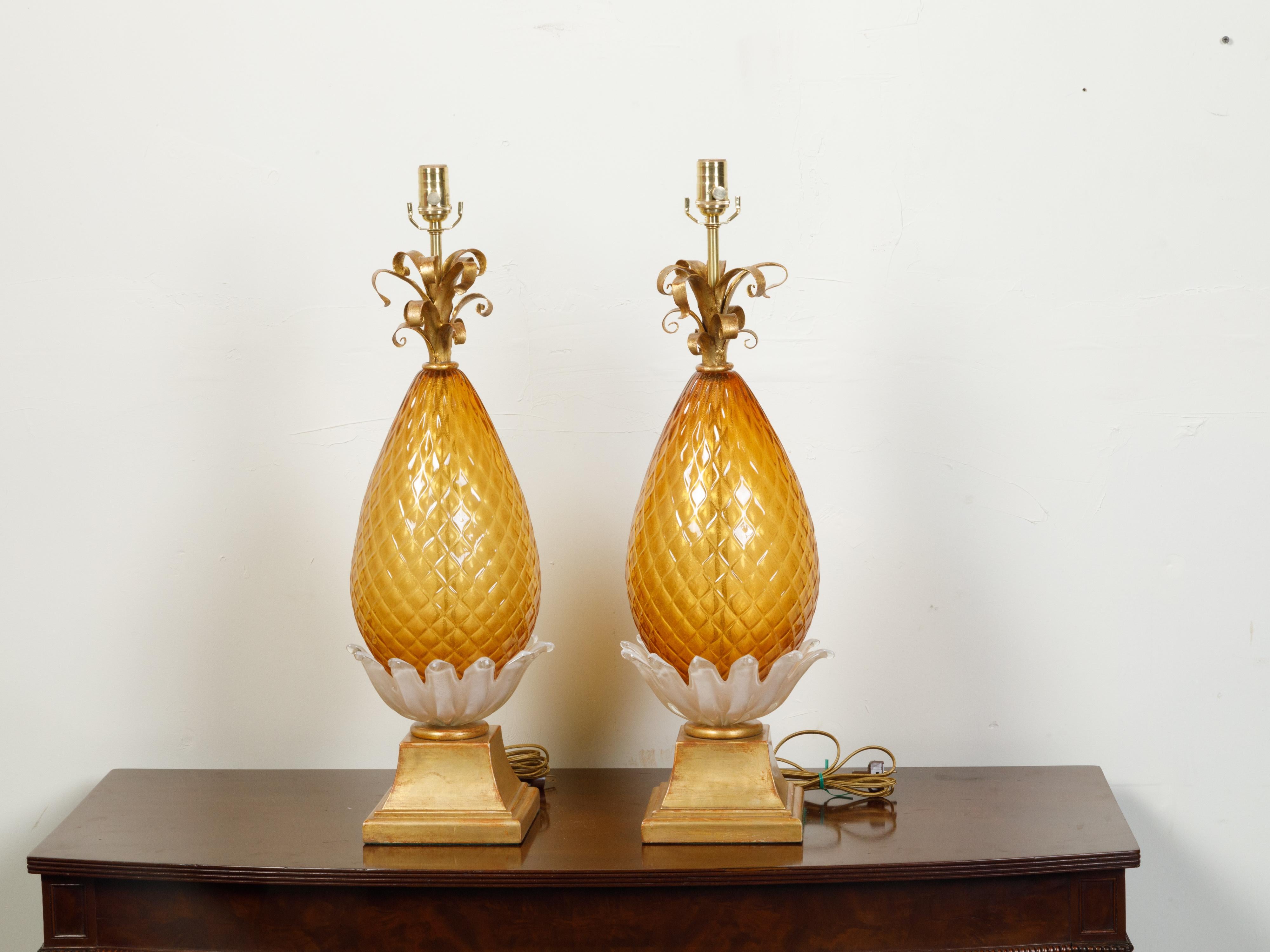 A pair of Italian Venetian Murano glass pineapple style table lamps from the 20th century, with cross-hatched motifs, gilt metal scrolls and stepped bases. Created in Murano during the 20th century, each of this pair of table lamps attracts our