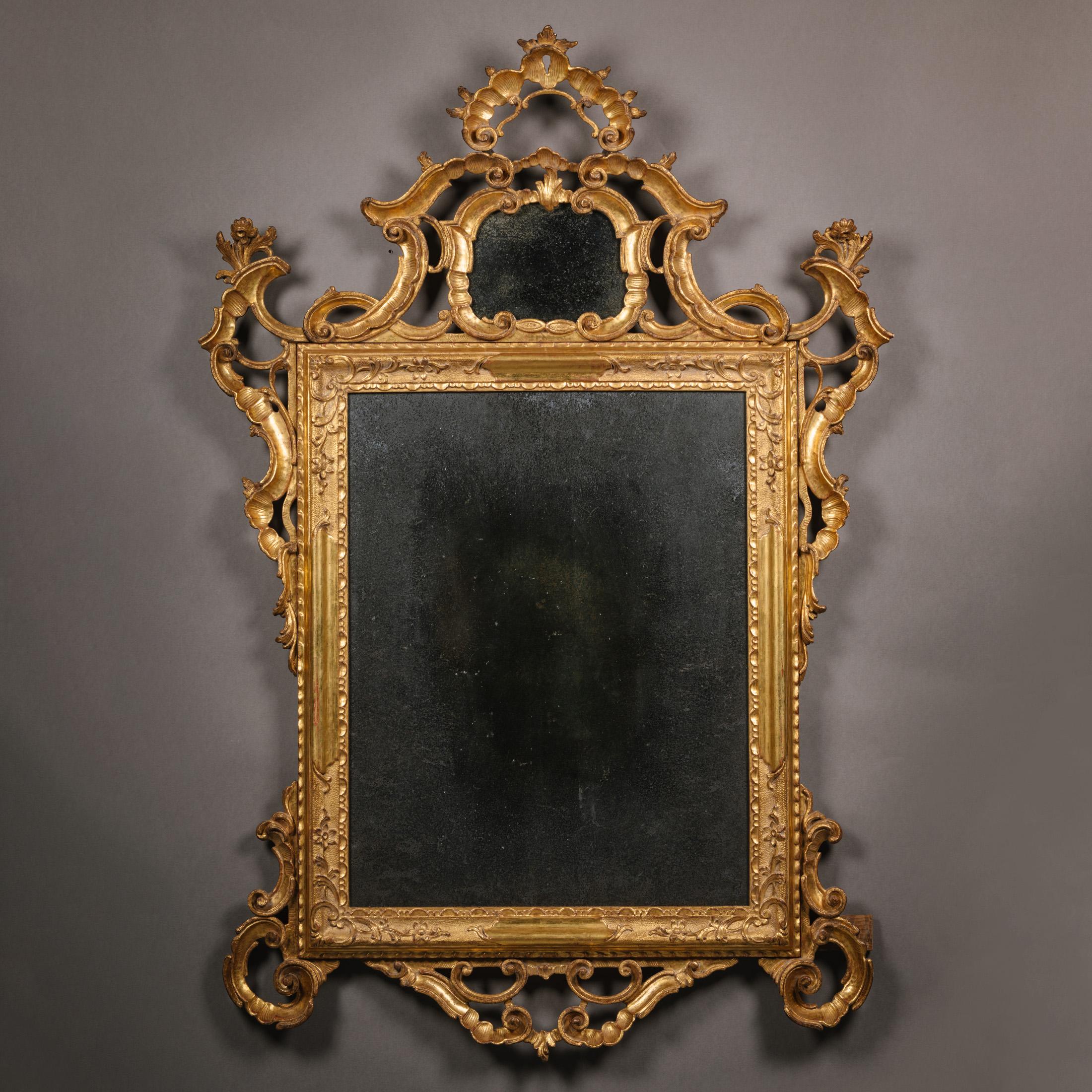 A Pair of Venetian Rococo Carved Giltwood Mirrors.  

These mirrors have elaborate pierced strapwork crestings surmounted by a shell-shaped corona above a cartouche-shaped plate, the rectangular mirror plates within a carved giltwood and gilt-gesso