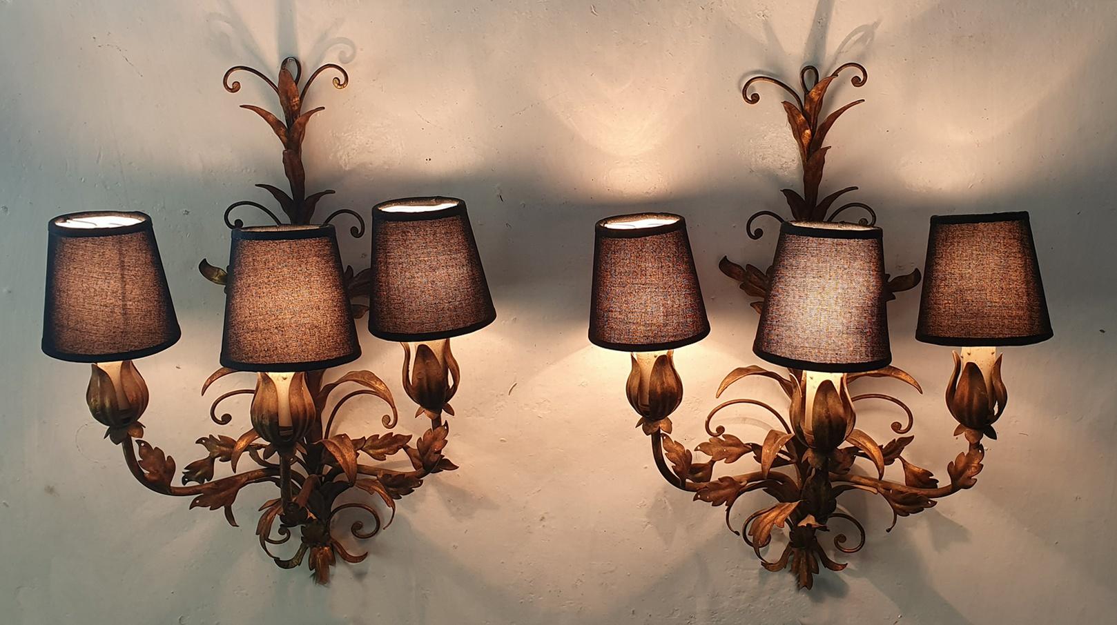 A pair of midcentury Venetian tole wall sconces, each with three lights each and decorated with gilded leaves. The candles are original and we have added brand new black lampshades with cotton fabric. The pair is in working condition and uses E14