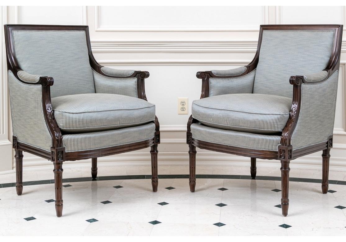 A stately pair of Club Chairs crafted by noted American maker Hancock & Moore. Dark mahogany frames with tall square backs, closed carved sloping arms with scrolled ends. The lower arms with carved leaves and with slightly curved seat rails. Raised