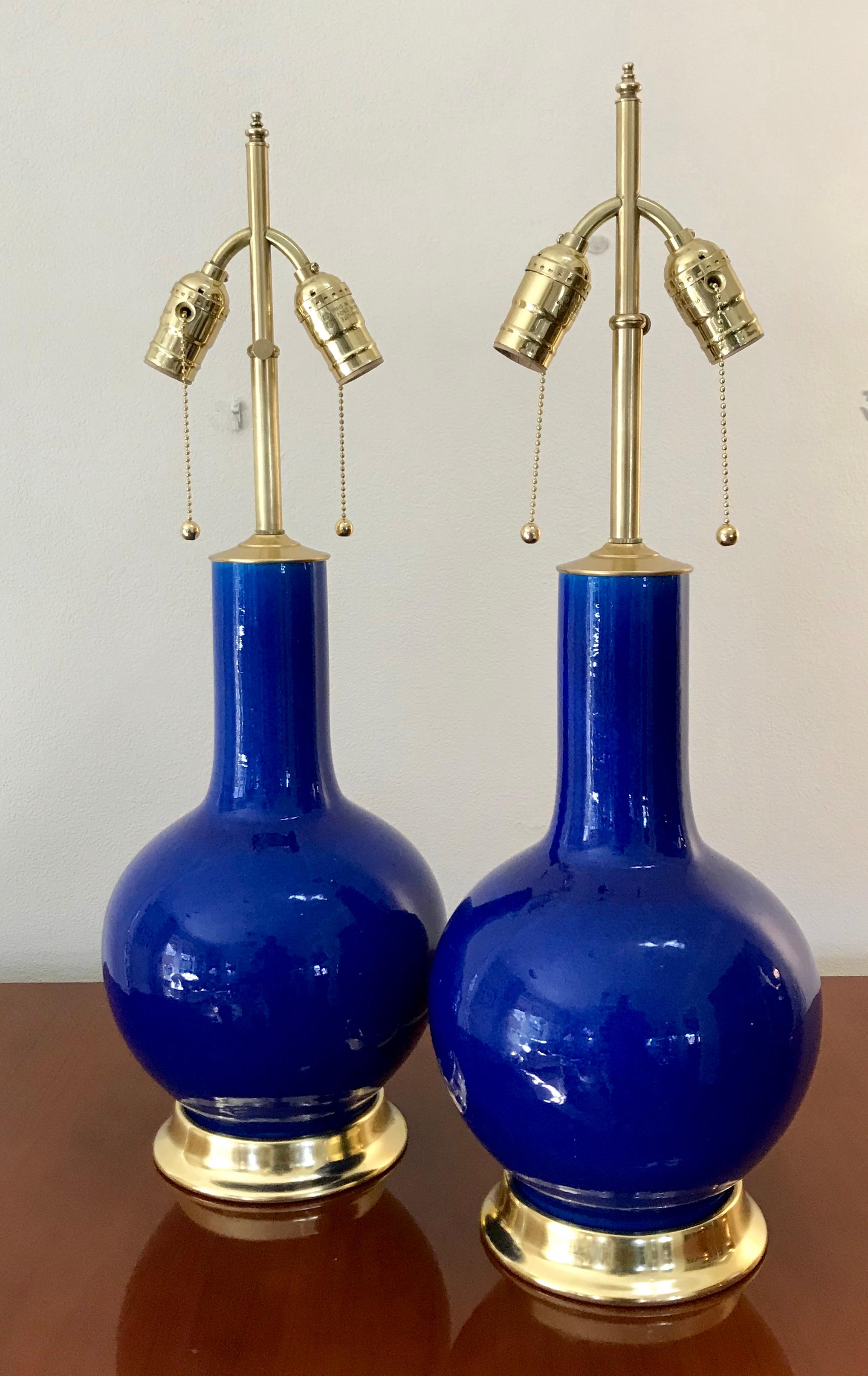 Pair of Chinese export globular or single gourd form porcelain vases converted to lamps mounted on custom wood turned bases in a 23 karat double water gilt finish. The eye catching blue color is very vibrant and has a very reflective and glassy