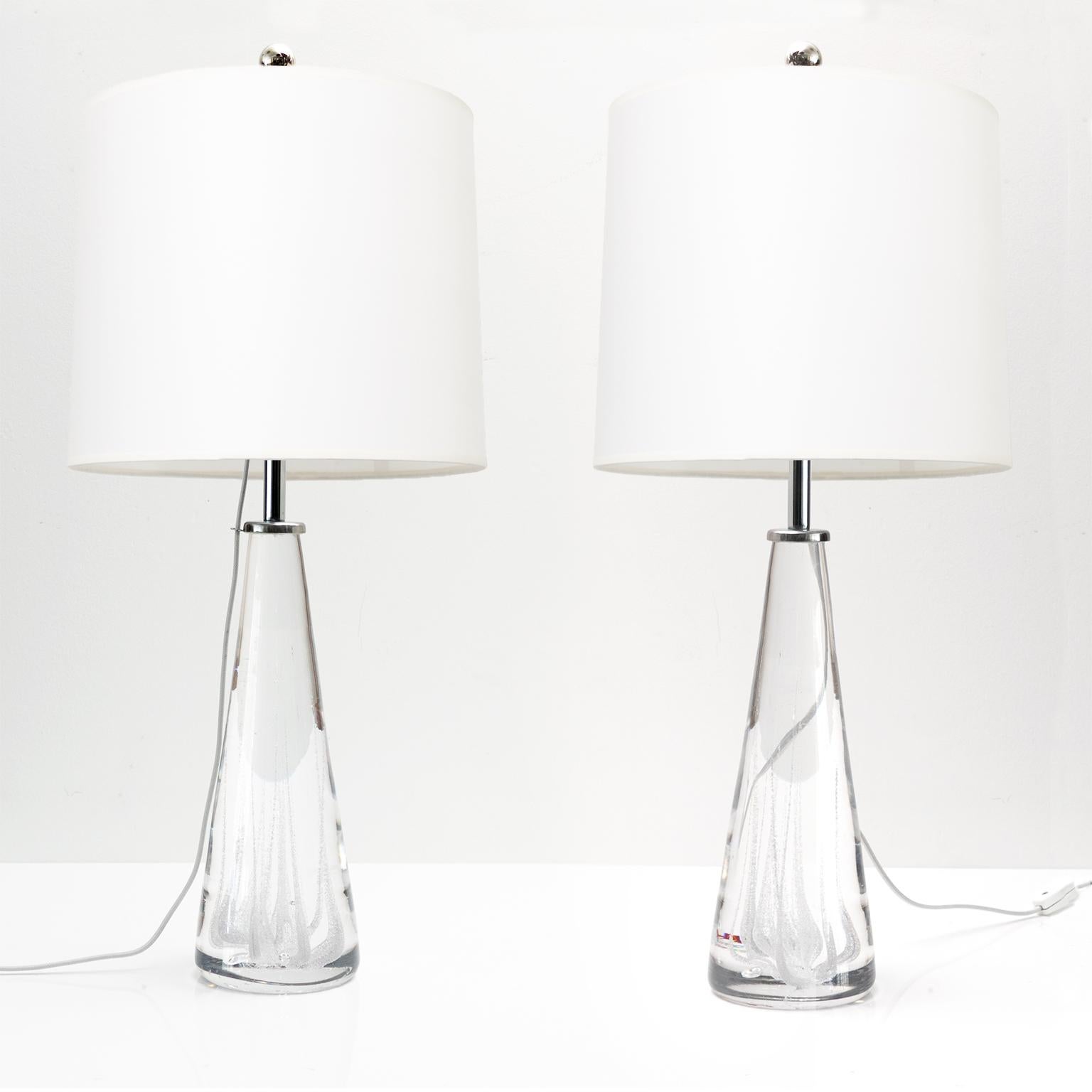 Pair of Scandinavian Modern solid crystal glass tables lamps made by one of Sweden's top glass producers, Kosta. The lamps are detailed with internal streaks of air bubbles and fitted with polished steel hardware and a single standard base 3-way