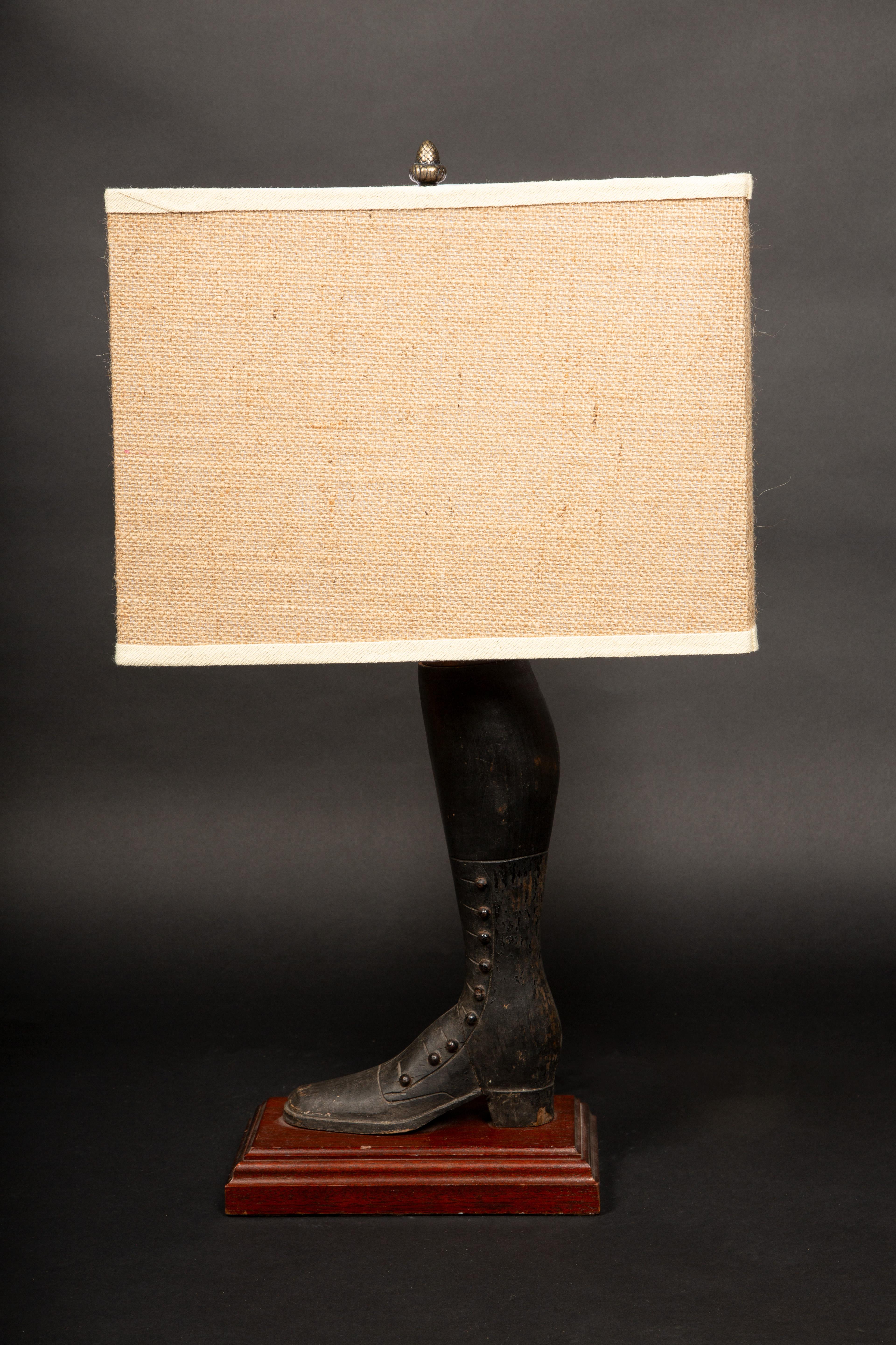 This striking pair of lamps features a unique and whimsical design inspired by Victorian-era fashion. The base of each lamp is exquisitely carved from wood in the form of a finely detailed boot, reminiscent of the elegant, lace-up footwear popular