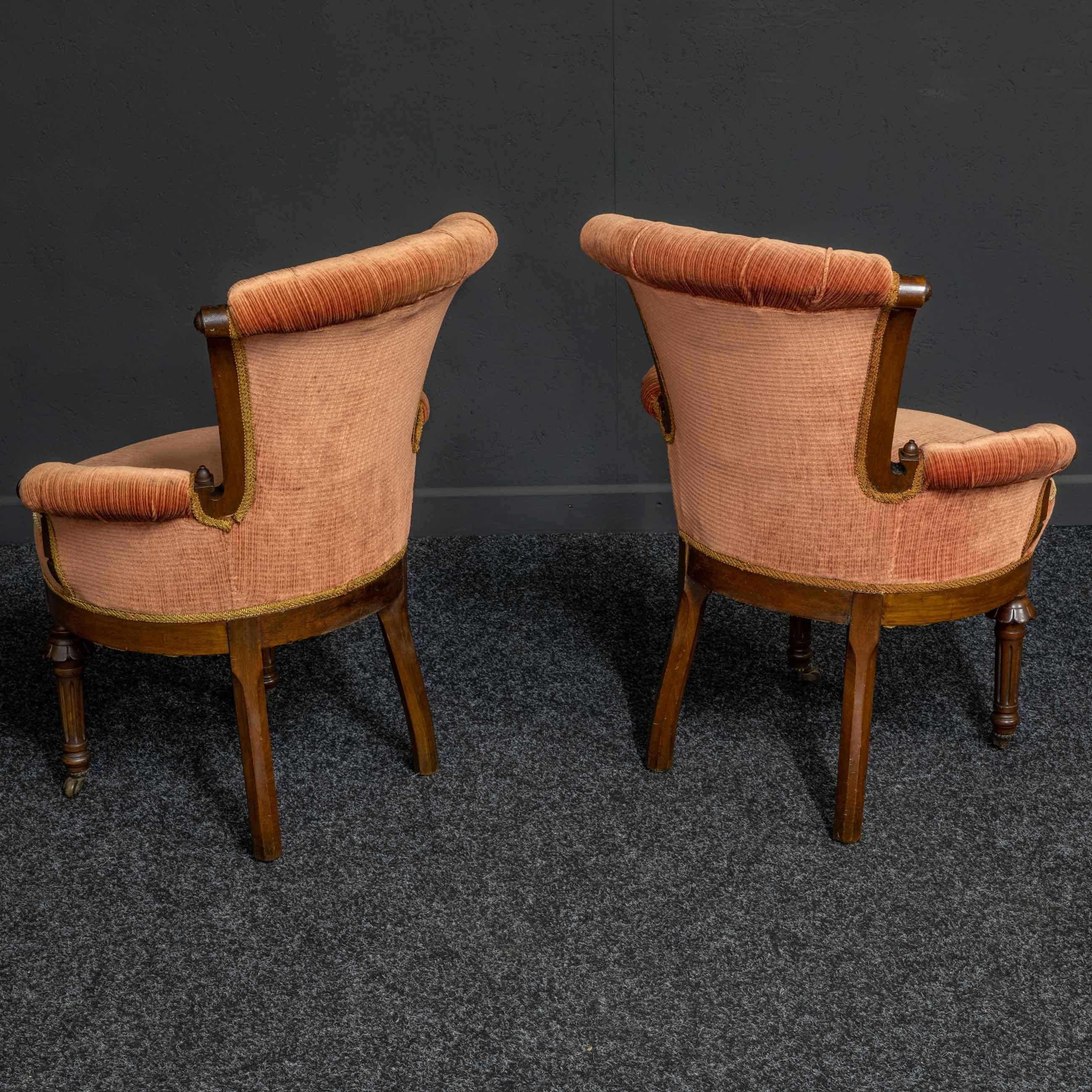 A pair of Victorian boudoir chairs of small proportions. Made from English walnut and remarkably sturdy. The upholstery is probably from the 1970s and is in very good order for it's age and still serviceable. The chairs are round in shape with a