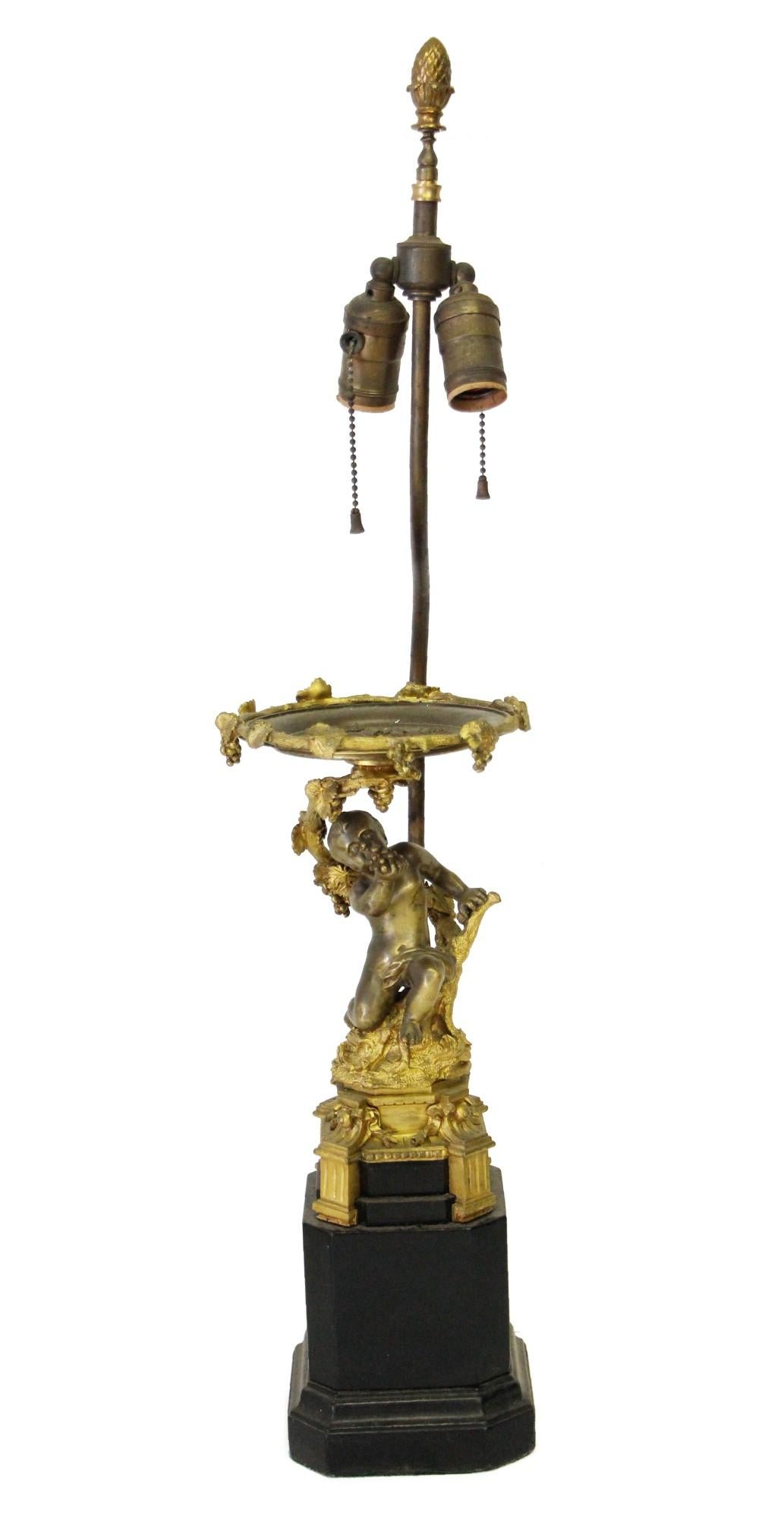 Pair of Victorian cherubic ornate brass table lamps with two lights each. Features a black base to complete the look. Priced as a pair. This can be seen at our 302 Bowery location in NoHo in Manhattan.