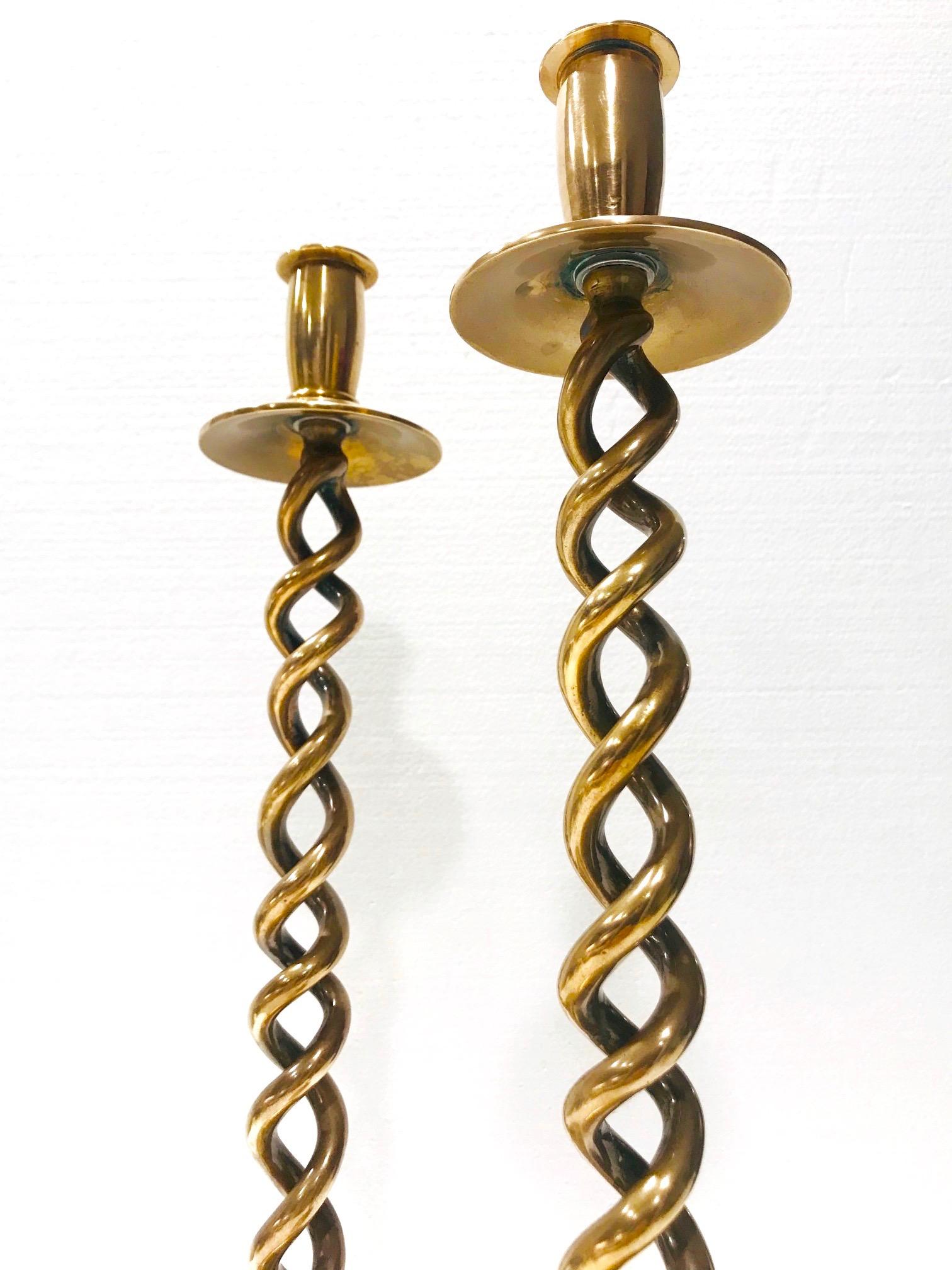 Pair of tall candleholders in cast brass metal. The antique candlesticks have open braided stems with a classic barley twist design and feature circular stepped bases. Solid weight with polished brass finish in hues of gold copper. Minor patina on