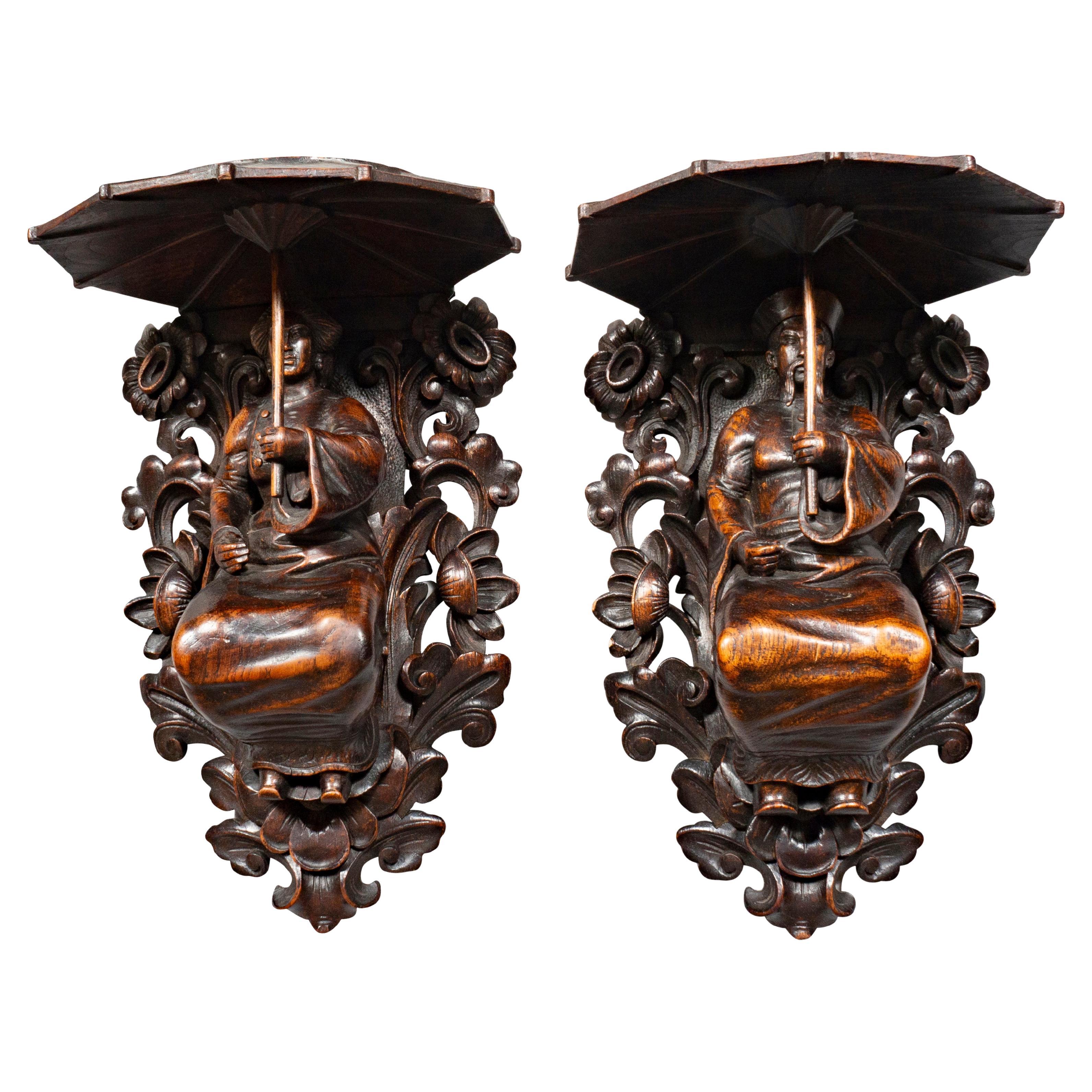 Each nicely carved figures of an Asian man and woman holding parasols with flat tops. Each surrounded by floral and leaf carving.
