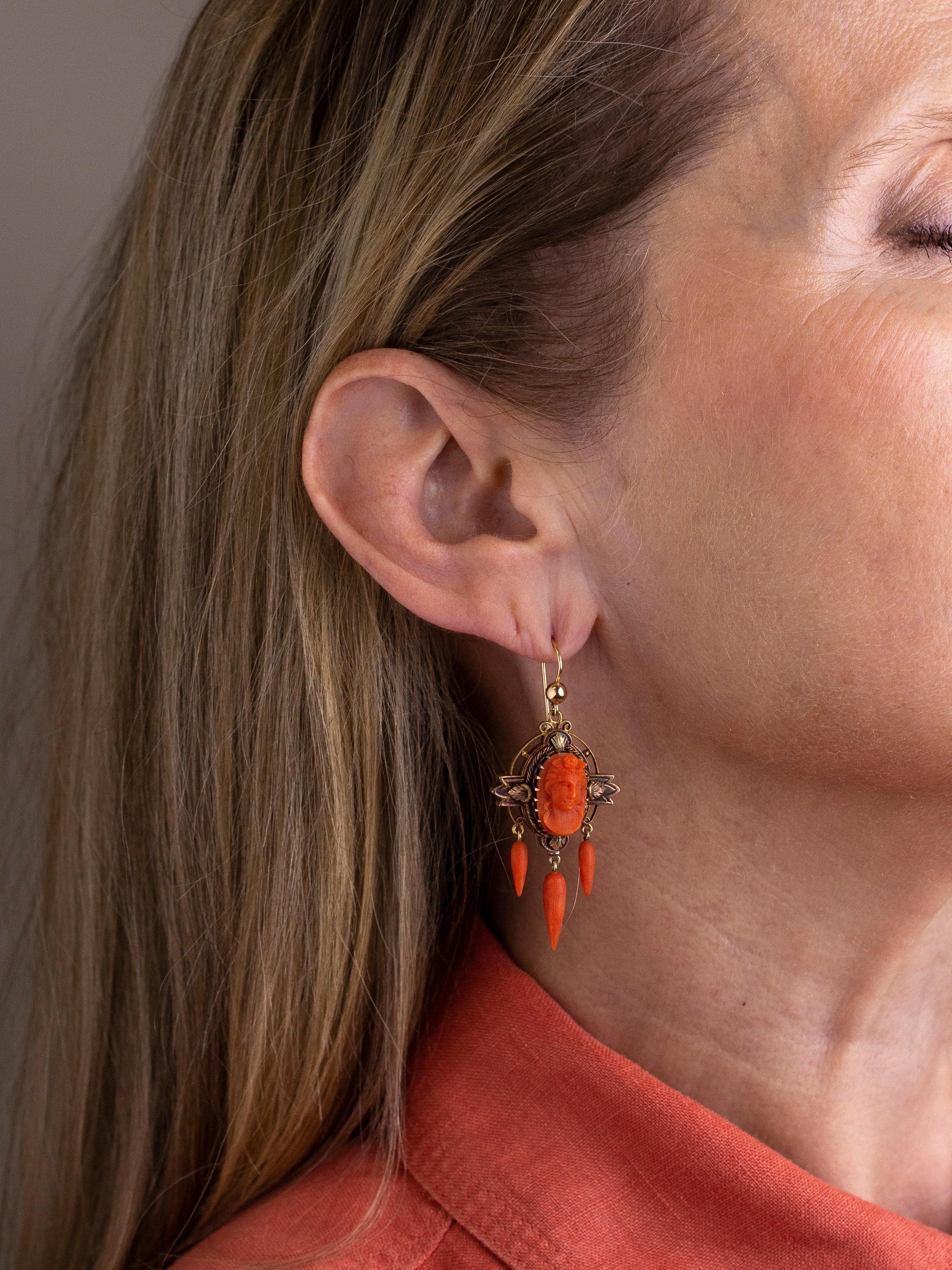This pair of 18 karat gold and coral drop earrings are High Victorian in terms of their age and appearance and are a beautiful example of 19th century craftsmanship. The pair each centre on an oval cameo of a woman carved from natural coral which