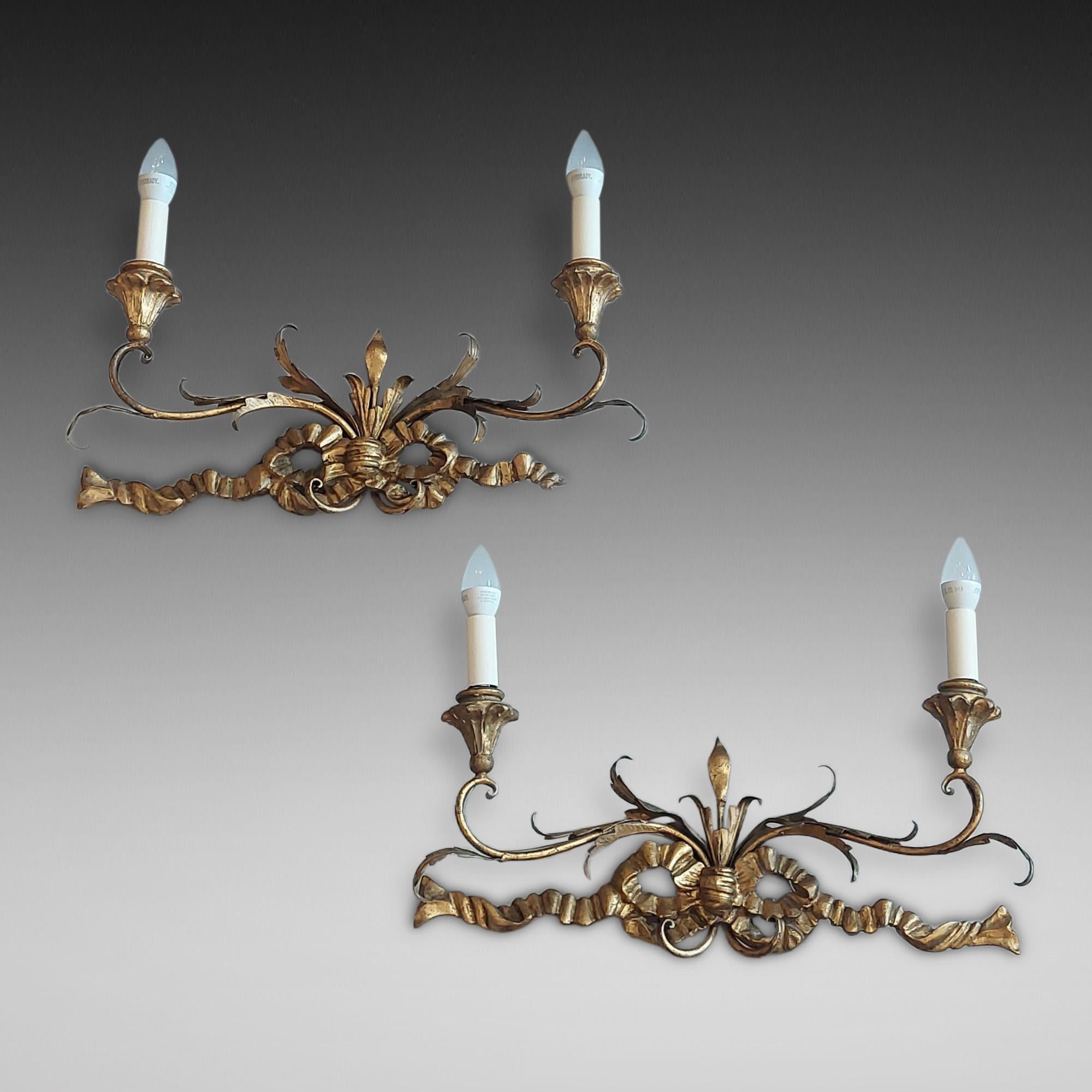 Pareja de apliques victorianos de dos brazos de madera dorada, cada apliques tallado con un lazo de cinta que emite unos brazos en forma de voluta rematados en hojas - originalmente para velas, ahora convertidos a eléctricos - 21 