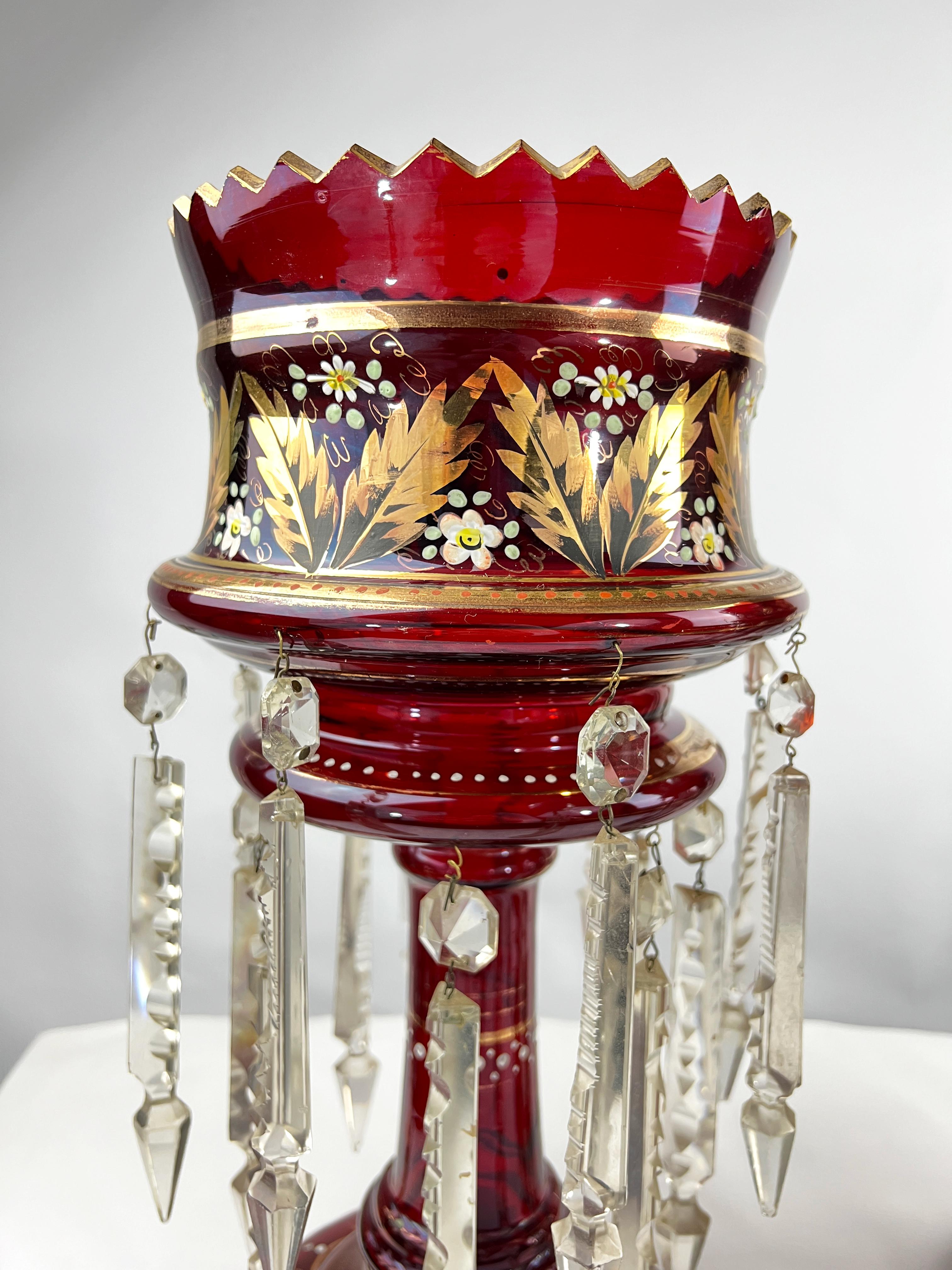 Pair of late 19th century ruby glass Lusters decorated with enamelled flowers and gilded leafs, each with double row of cut glass drops, raised on round bases.
 
