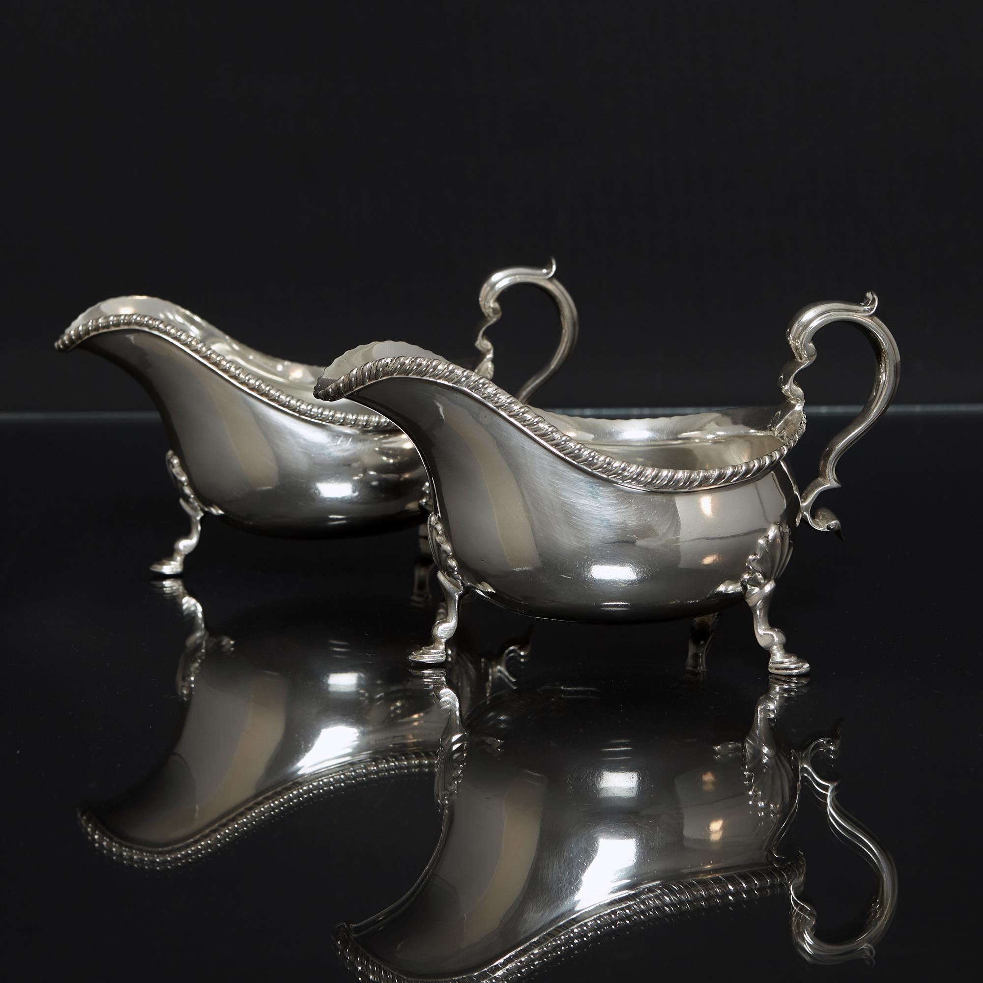 Pair of large George III style silver gravy boats with applied slant gadroon pattern borders. Each boat has cast leaf-capped scroll handles and three legs with stylised shell bolsters and hoof supports.

While some vessels have been identified as
