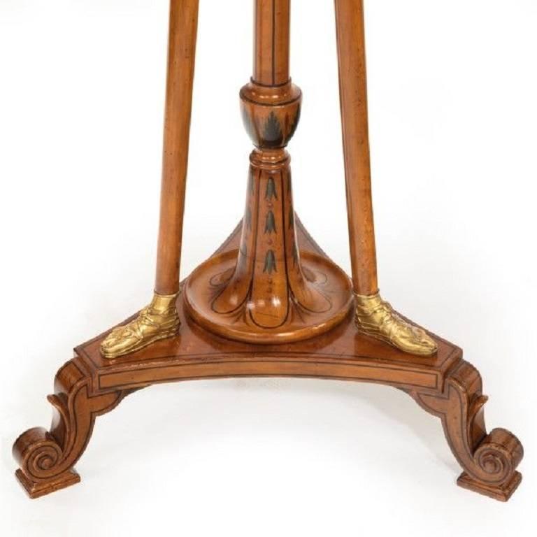 A pair of late Victorian painted satinwood and ormolu tripod stands,
each with a circular tray set on a turned support with a tripod base with three scroll feet, all within three female term brackets which have painted gilt faces and simulated