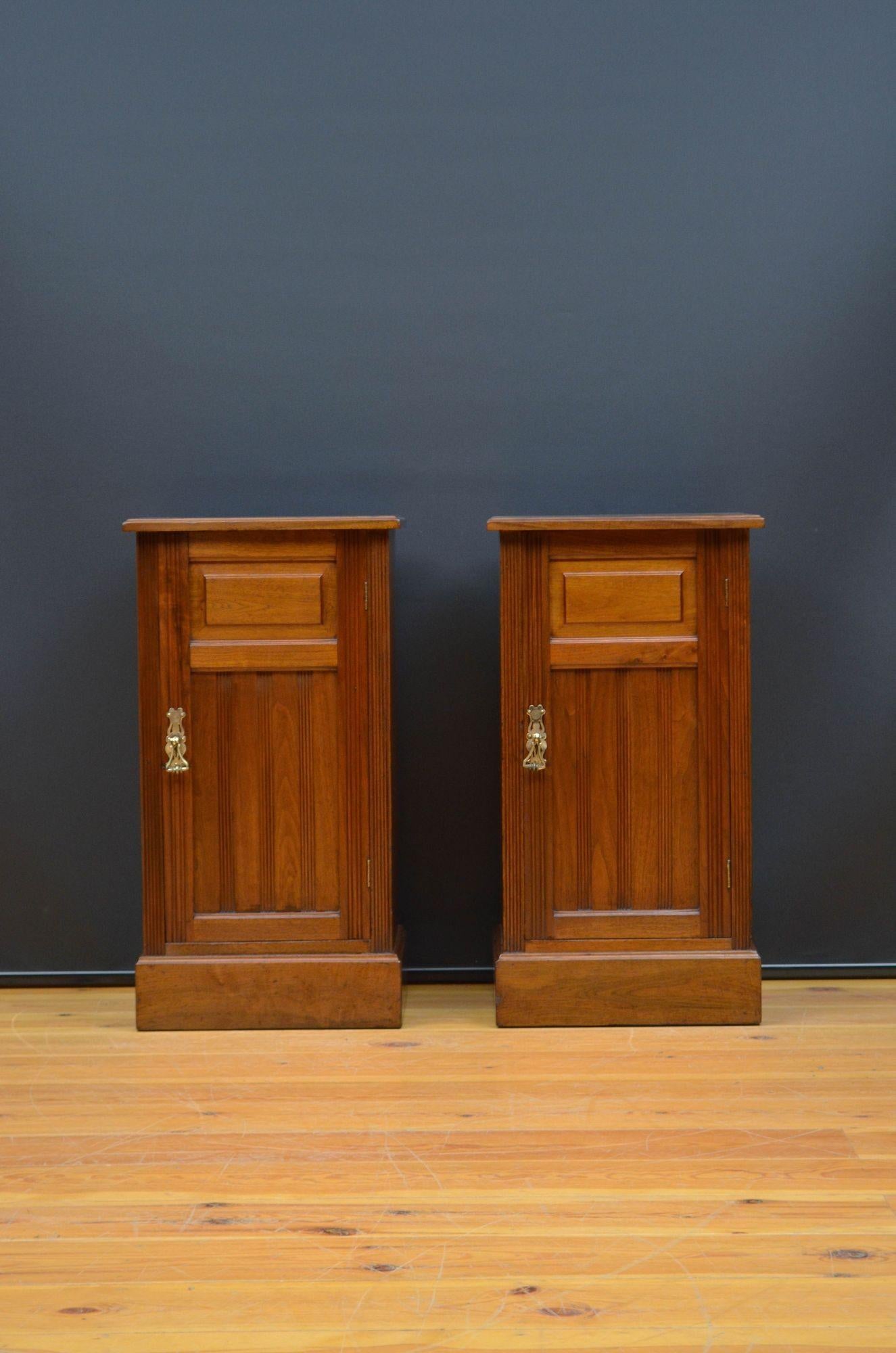 Sn5580 Pair of antique bedside cupboards in walnut, each having figured walnut top with moulded edge above fielded, fluted carved and panelled cupboard door fitted with original brass handle and enclosing a shelf, all standing on moulded plinth