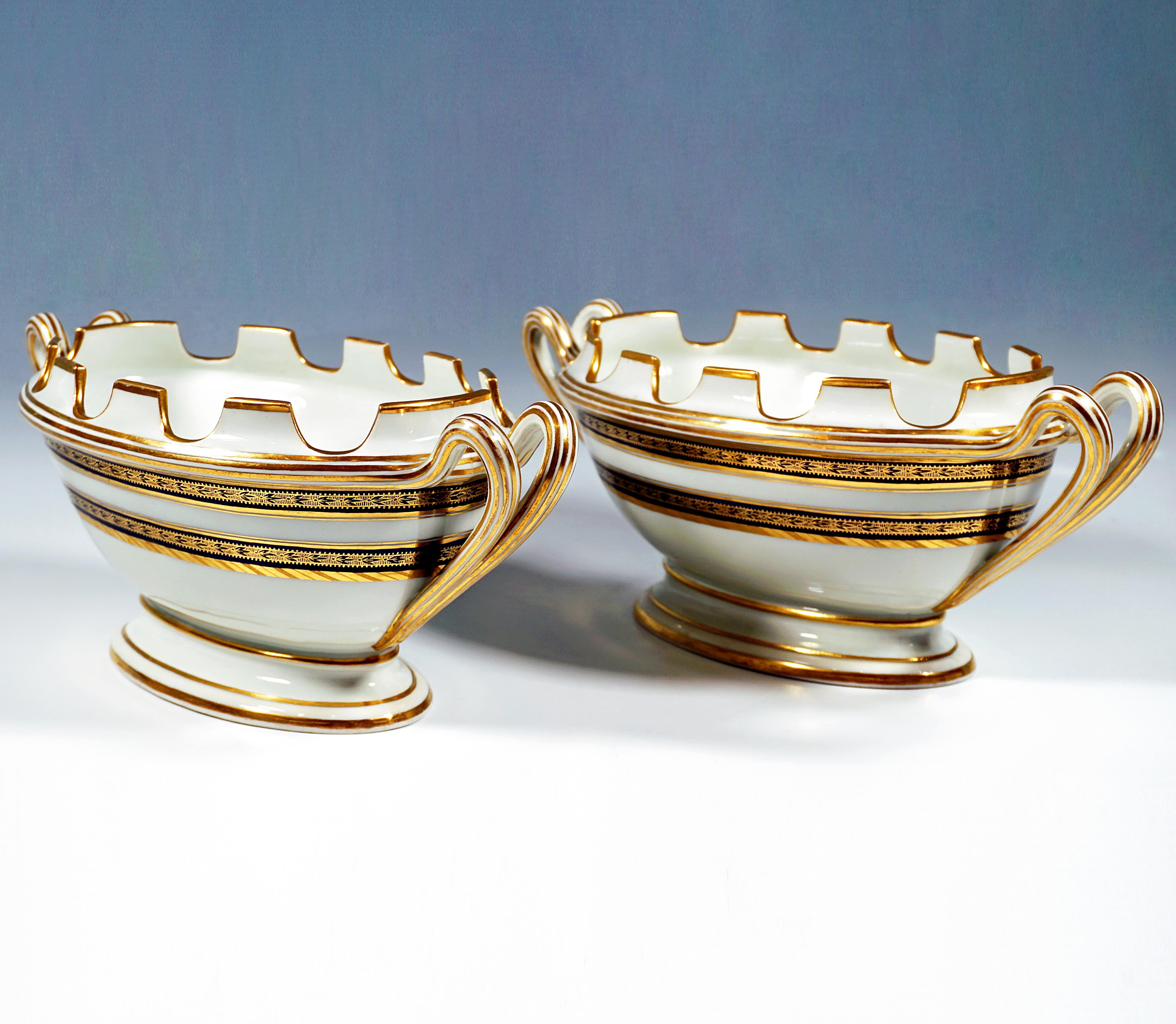 Raro par de elegantes vasijas ovaladas de porcelana sobre pies desplazados y acanalados, con paredes abombadas y elevadas, borde acanalado y dentado de abertura recta con diez pequeños segmentos recortados en forma de almenas para guardar el vidrio,