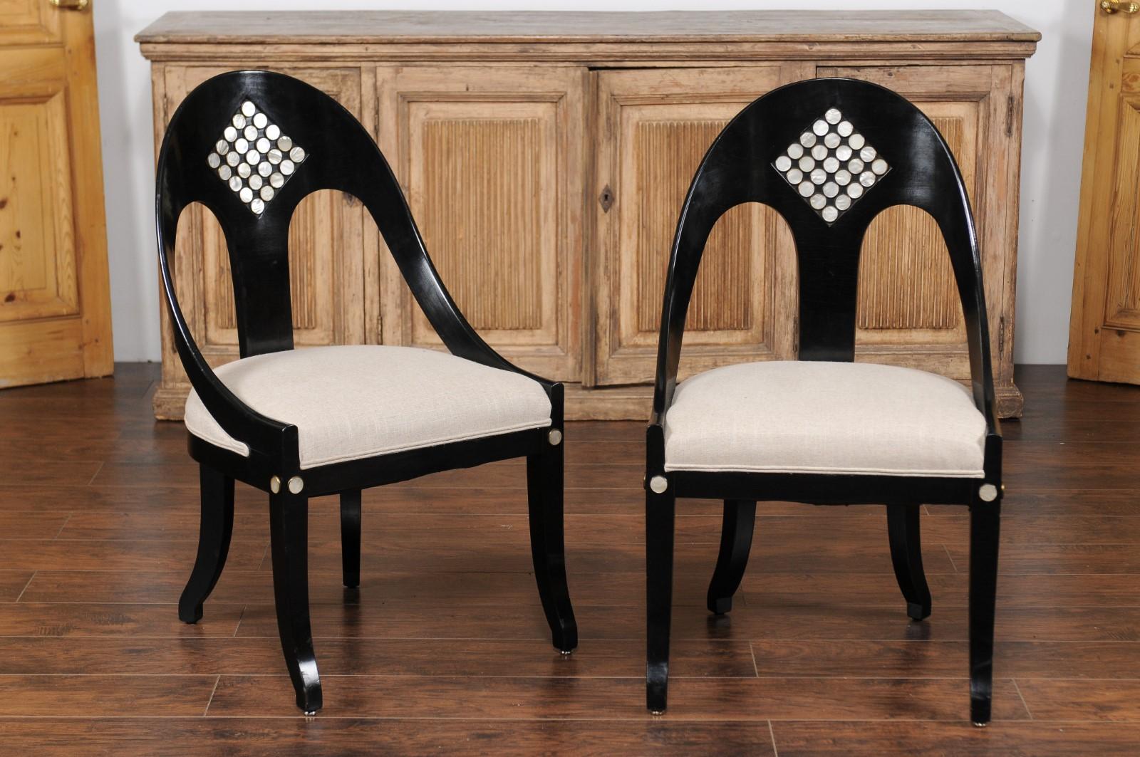 A pair of vintage American ebonized wood spoon back chairs from the mid 20th century, with mother of pearl inlay and newly upholstered seats. Born during the midcentury period, each of this pair of ebonized chairs features a pierced spoon back,