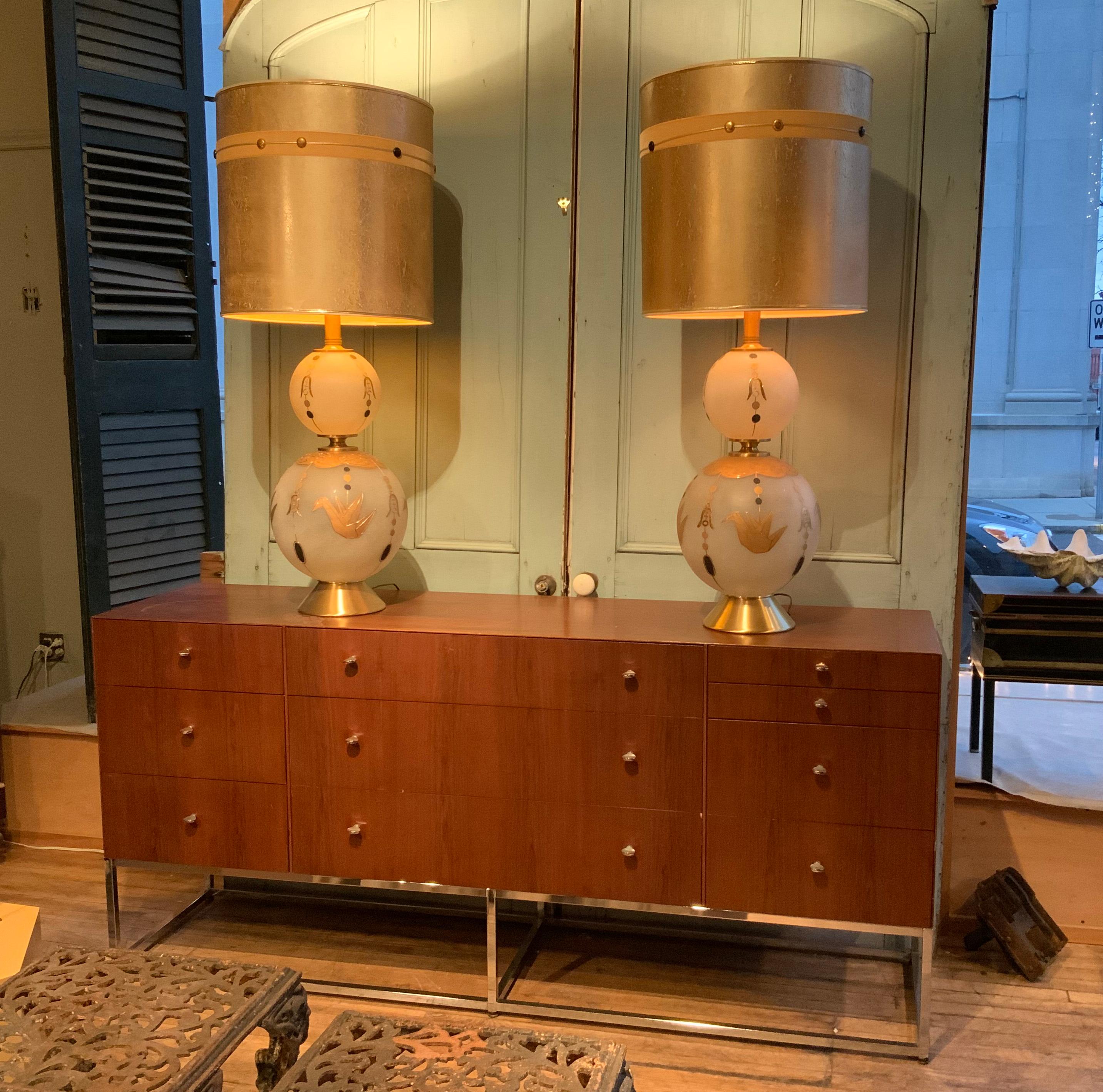A beautiful and unique pair of vintage 1950's table lamps, with large bases made from graduated and frosted glass spheres, embellished with gold embossed doves and decorations, and raised on brass bases. together with their original gold wash