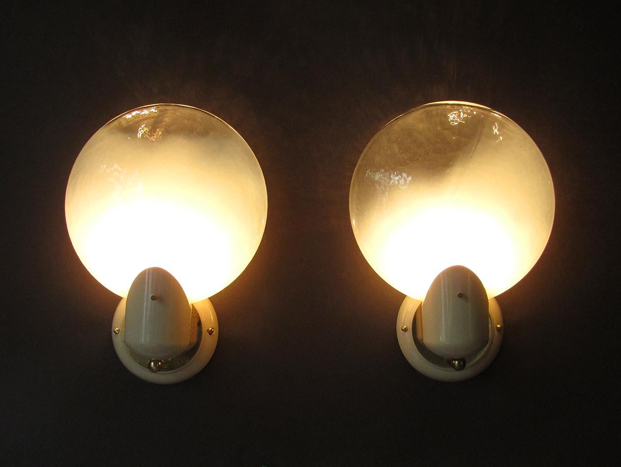 A pair of rare 1950s wall lights in Murano glass by Italian maker Gino Vistosi.

The large, thick glass shades cast a soft, diffused light.

They are mounted on brass and cream mounts of distinctly 1950s design.

In very good condition, there