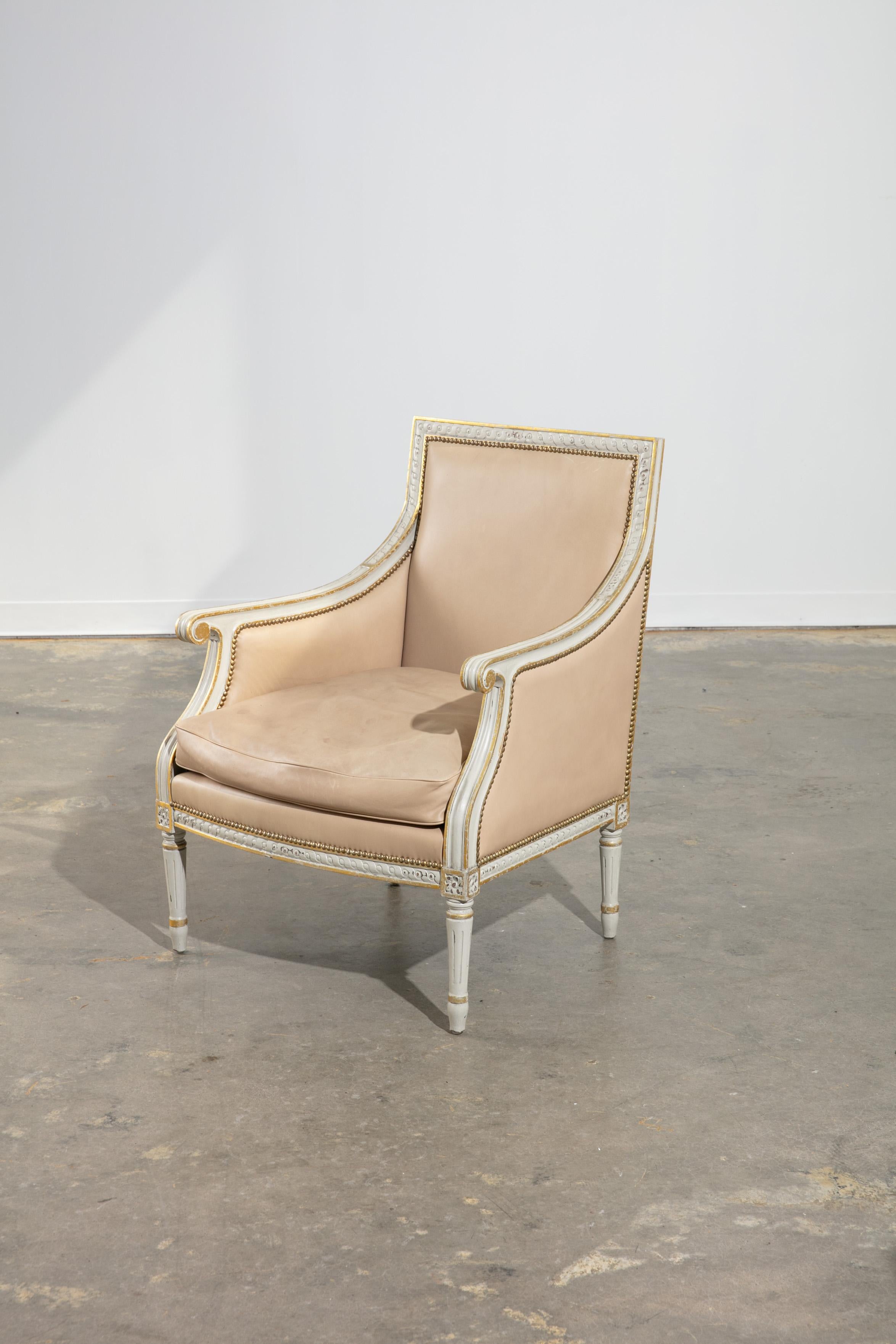 Pair of cream leather and gold and white painted armchairs with fluted legs and carved wood details throughout. Nice curved arm detail and nailhead trim . Chips to chair back and legs and markings throughout. In good vintage condition and
