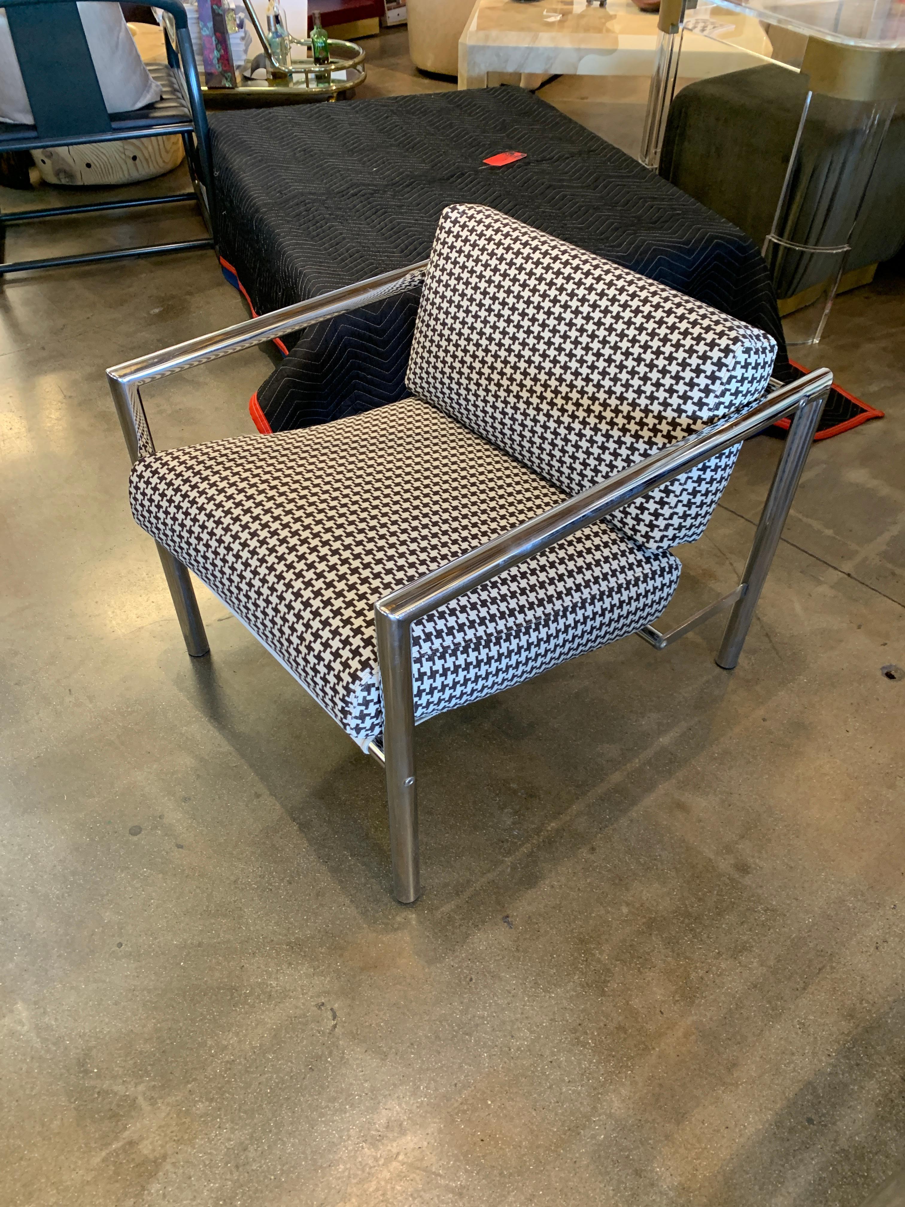 A pair of chrome frame lounge chairs from the 1970s re-upholstered in a houndstooth fabric. They feature canvas slings. The frames have an unusual shape by the bottom rear. The foam has been re-done as well. The chairs are in good vintage condition