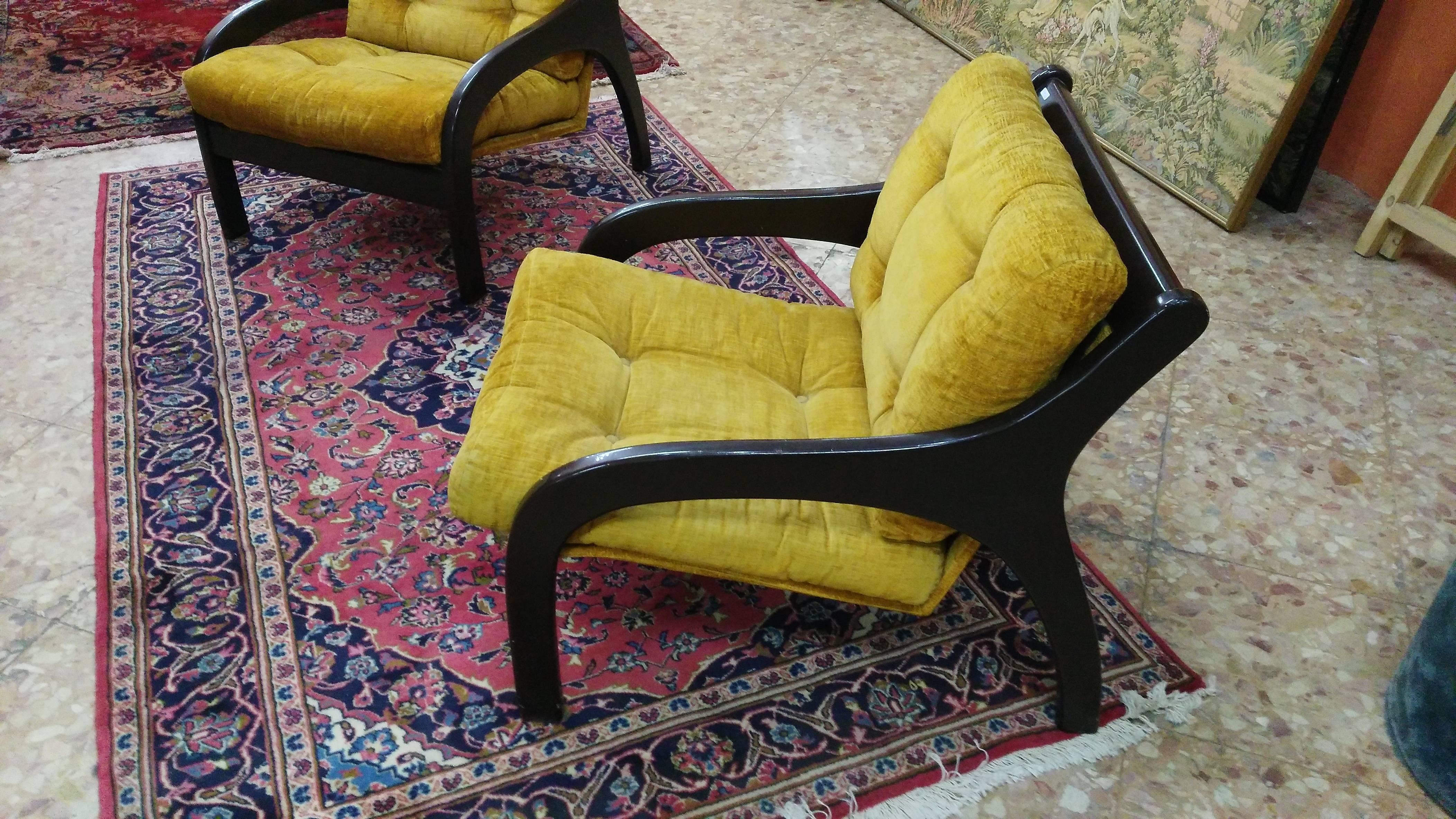 This vintage chair has a wooden structure and a yellow fabric lining. The wooden frame was finished and the cushions were dusted. The chair has large cushions and wooden armrests for added comfort.