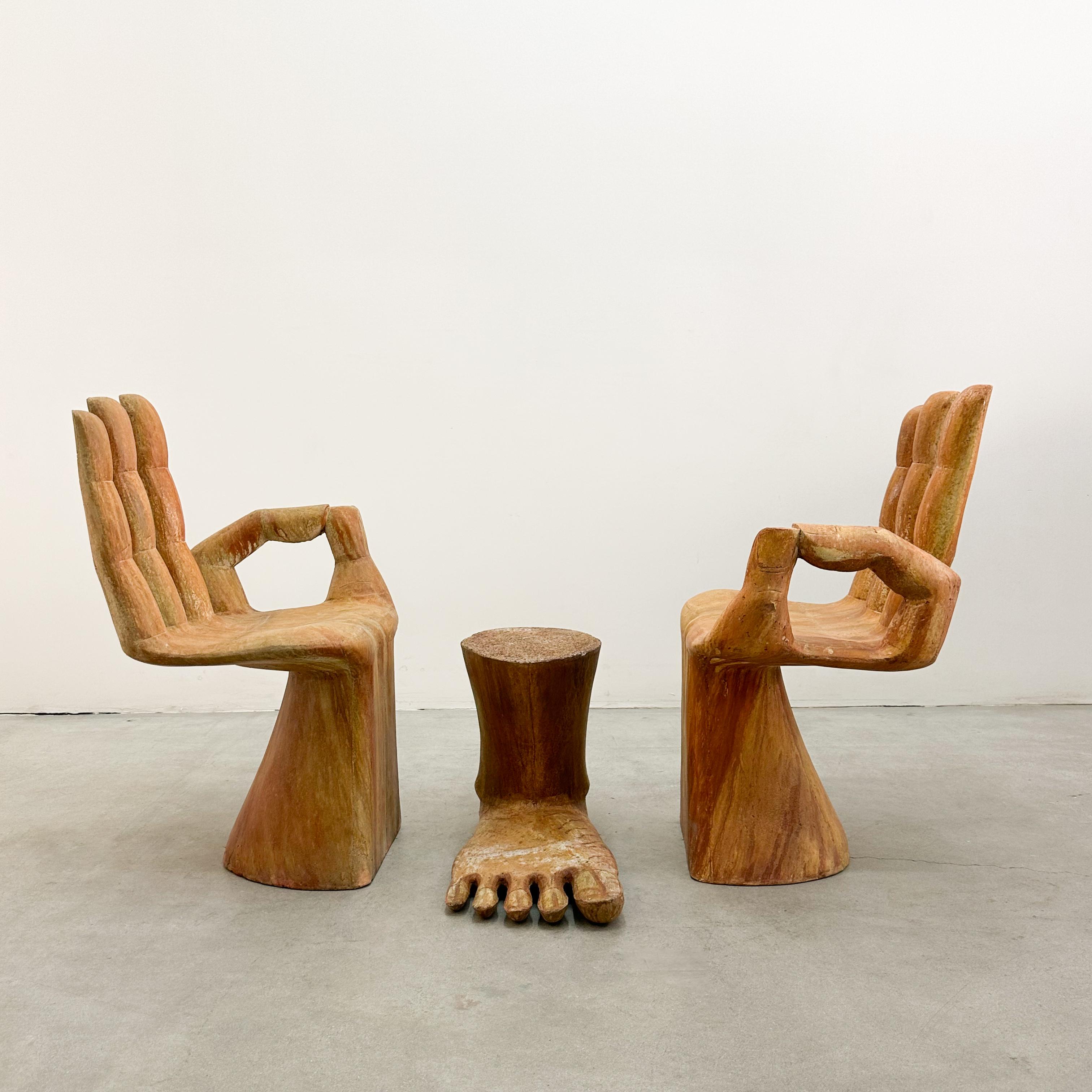 This unique pair of hand-shaped chairs with a matching foot table, designed in the 1970s, is crafted from a heavy concrete/plaster composite that mimics the look of natural wood. Inspired by the surrealist designs of Pedro Friedeberg, these