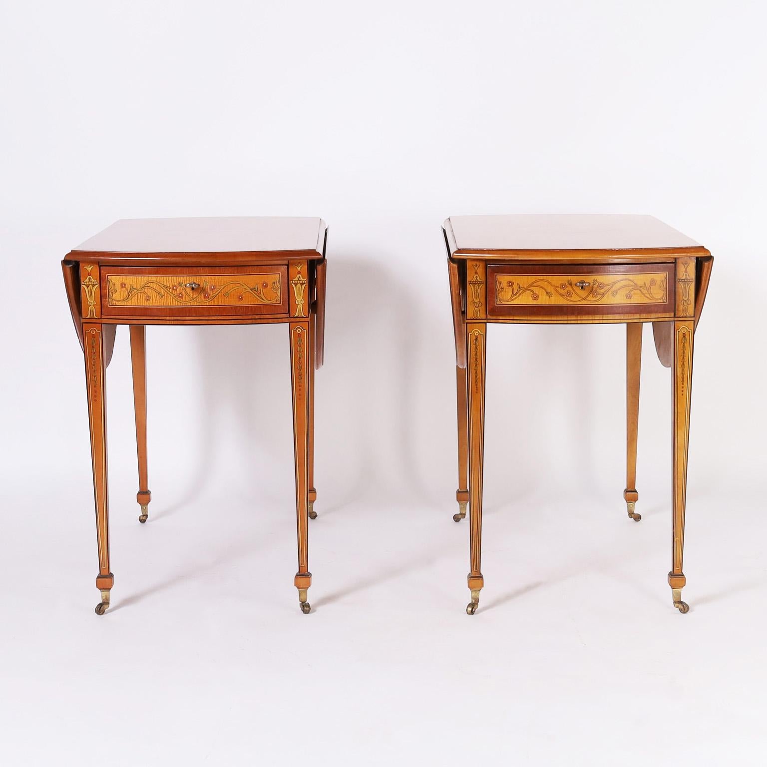 Dashing pair of one drawer drop leaf tables crafted in maple with mahogany cross banding in an elegant form with influences of Adam and Edwardian painted designs on long tapered legs with spade feet and brass casters. Tagged by the Historic New