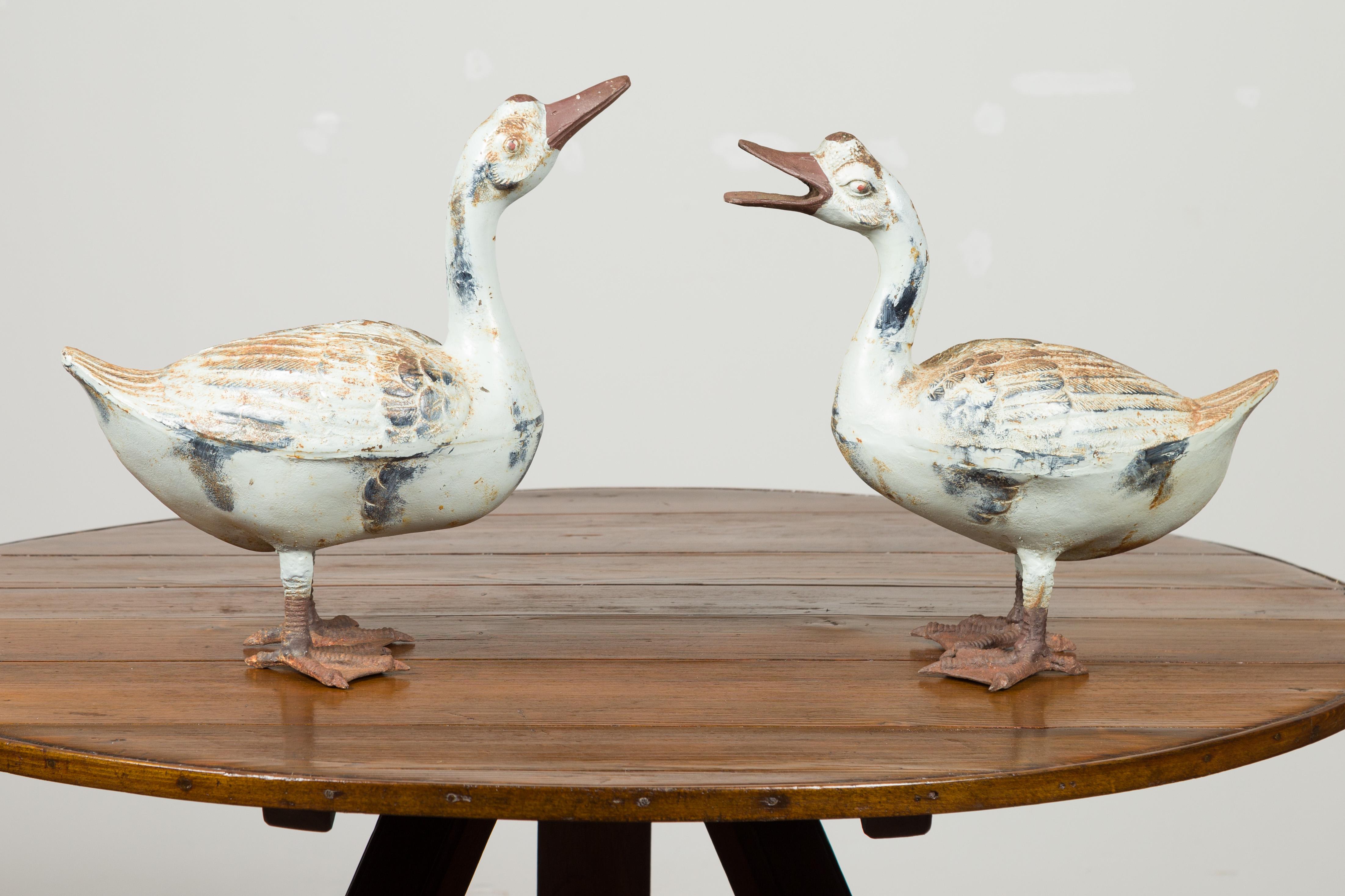 A pair of vintage American iron quacking ducks from the mid 20th century, with distressed patina. Made in the USA during the midcentury period, each of this pair or iron sculptures depicts a duck firmly planted on its palmate. A great sense of life