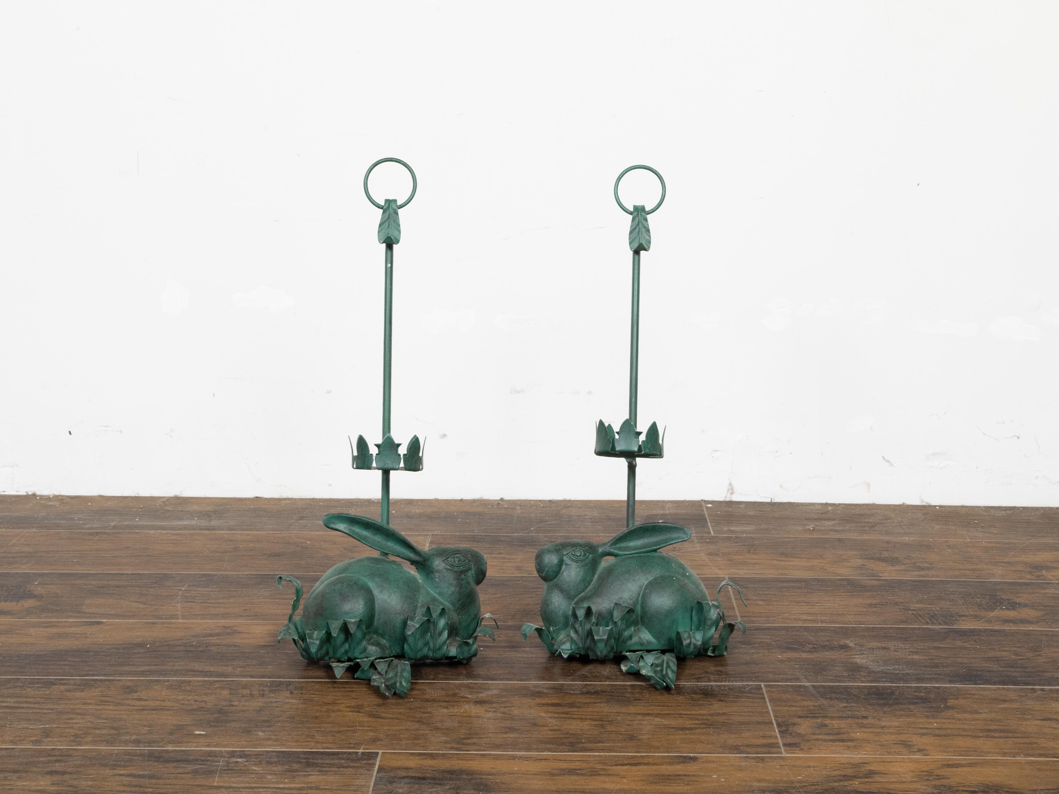 A vintage pair of American iron candle holders from the mid 20th century, with rabbit sculptures and green patina. Made in the USA during the Midcentury period, each of this pair of iron candle holders depicts a charming rabbit with its large ears