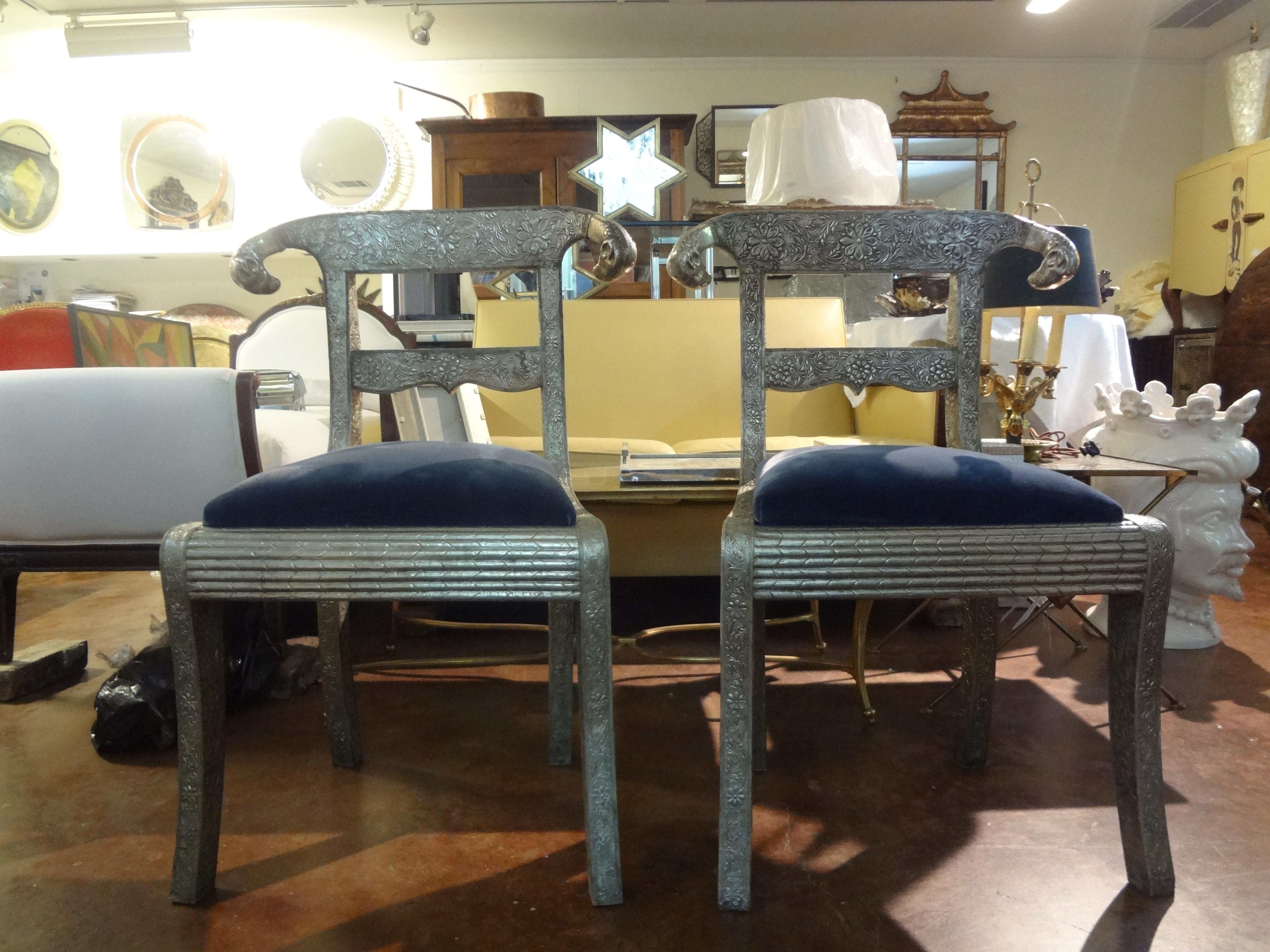Stunning pair of midcentury Anglo-Indian dowry side chairs with ram's head accents. These beautiful side chairs feature wooden frames clad in floral embossed silver metal and polished scrolling ram’s heads. The seats are upholstered in a lovely