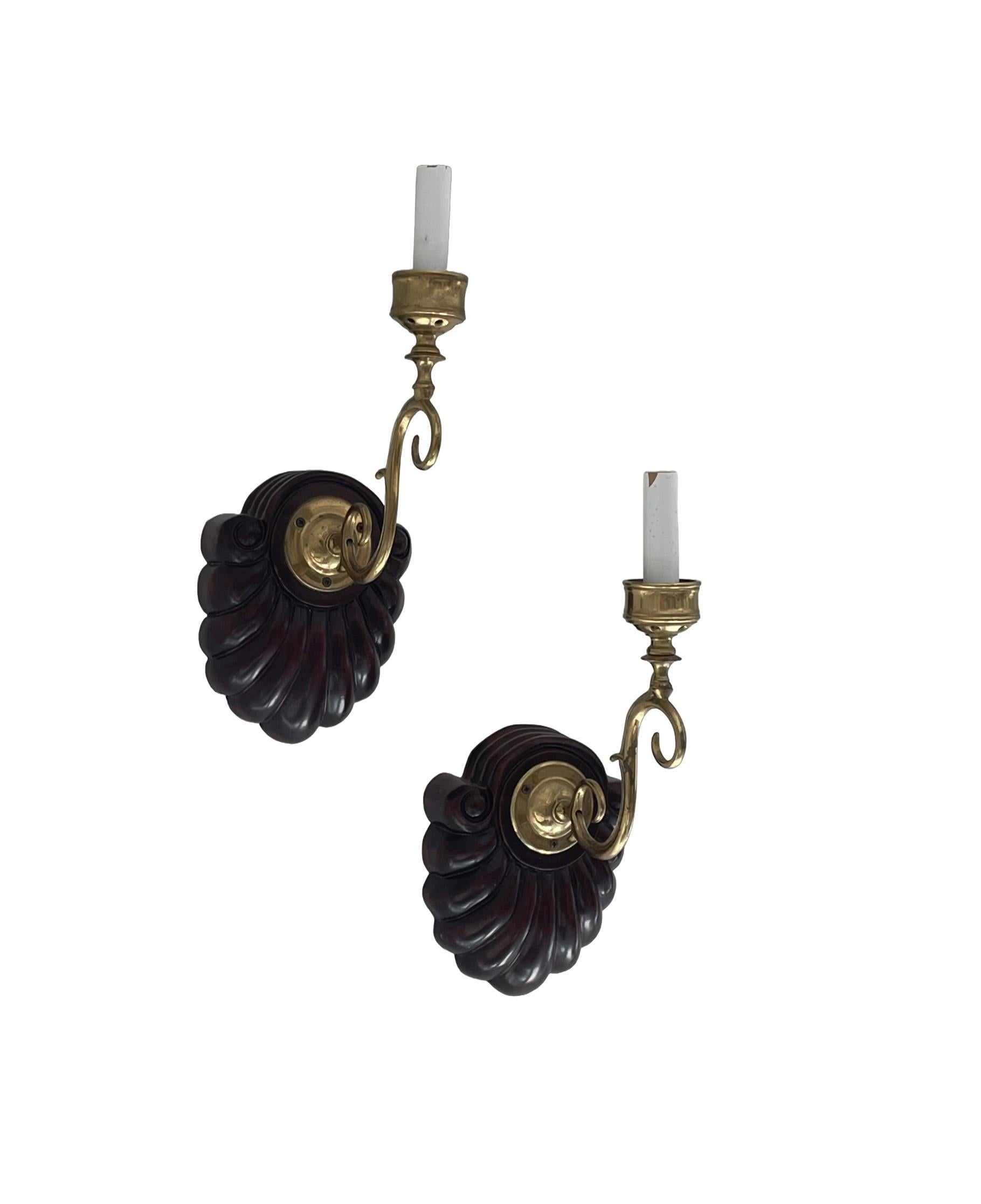 Make a statement with this pair of sophisticated and classic Anglo-Indian wall sconces. These hard-wired fixtures feature a carved shell form walnut backplate attached to a gracefully curled and patinated brass arm which holds the candle-style light