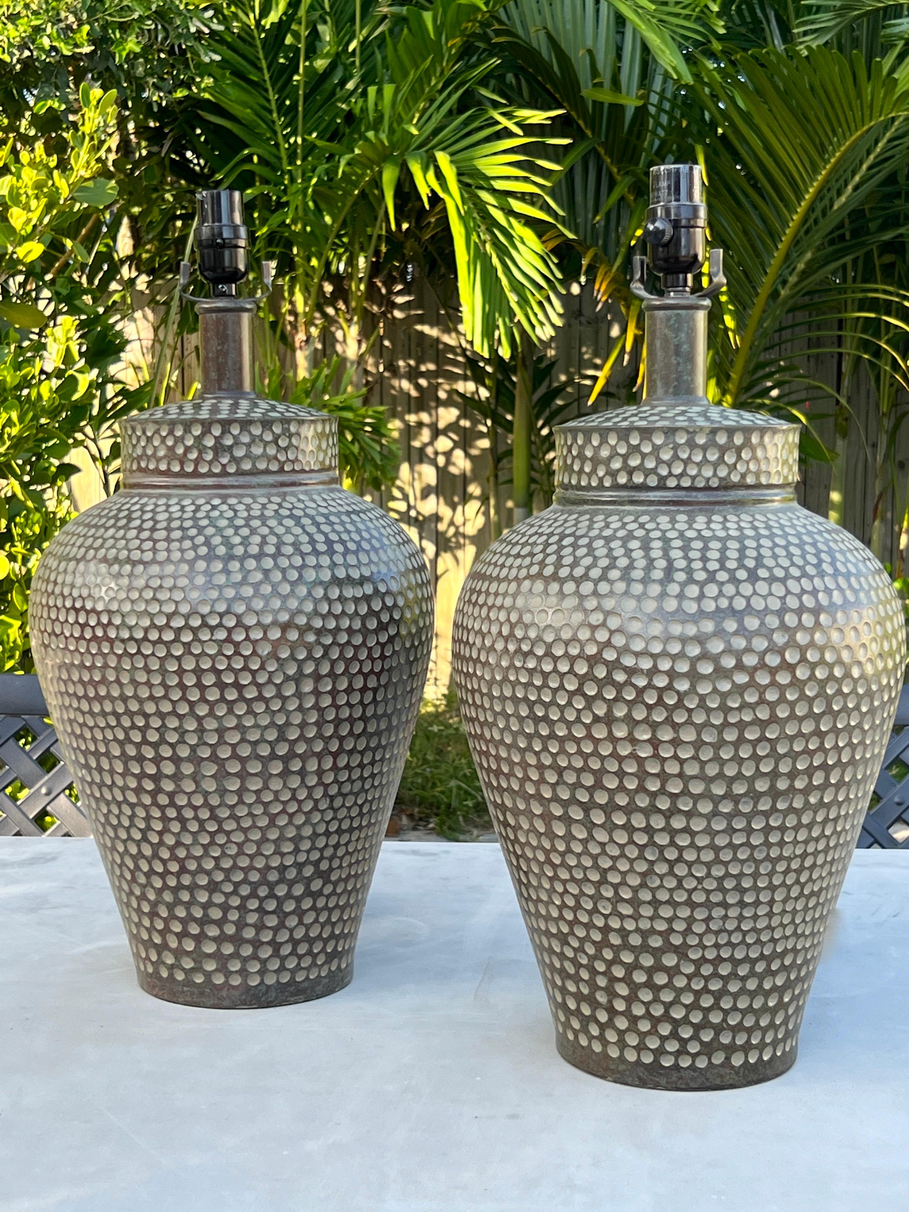 Pair of Chinese ginger jar lamps with hammered circles.  The lamps have urn forms comprised of hand painted resin with an antique patina finish.  Fitted with bronze metal stems and custom lamp shades in ivory linen. 