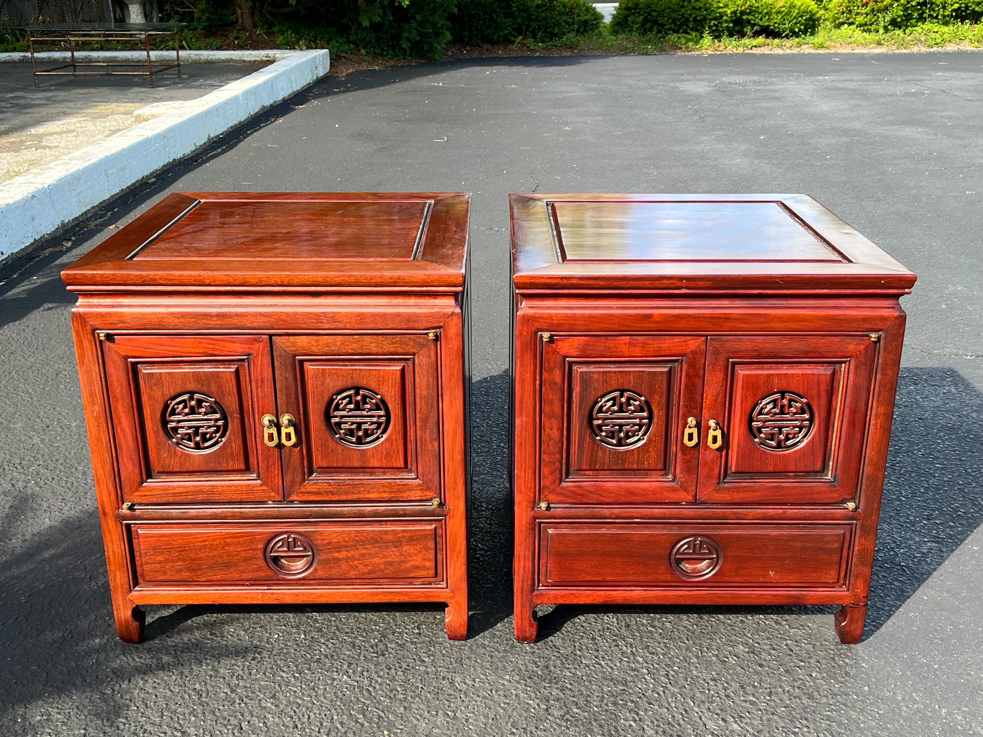 Pair of carved Asian rosewood nightstands with double door cabinet over singular lower drawer . Most likely by George Zee.Intricate mandarin carvings and exquisite detail. Nice brass tone hardware. These cabinets were photographed in the bright sun