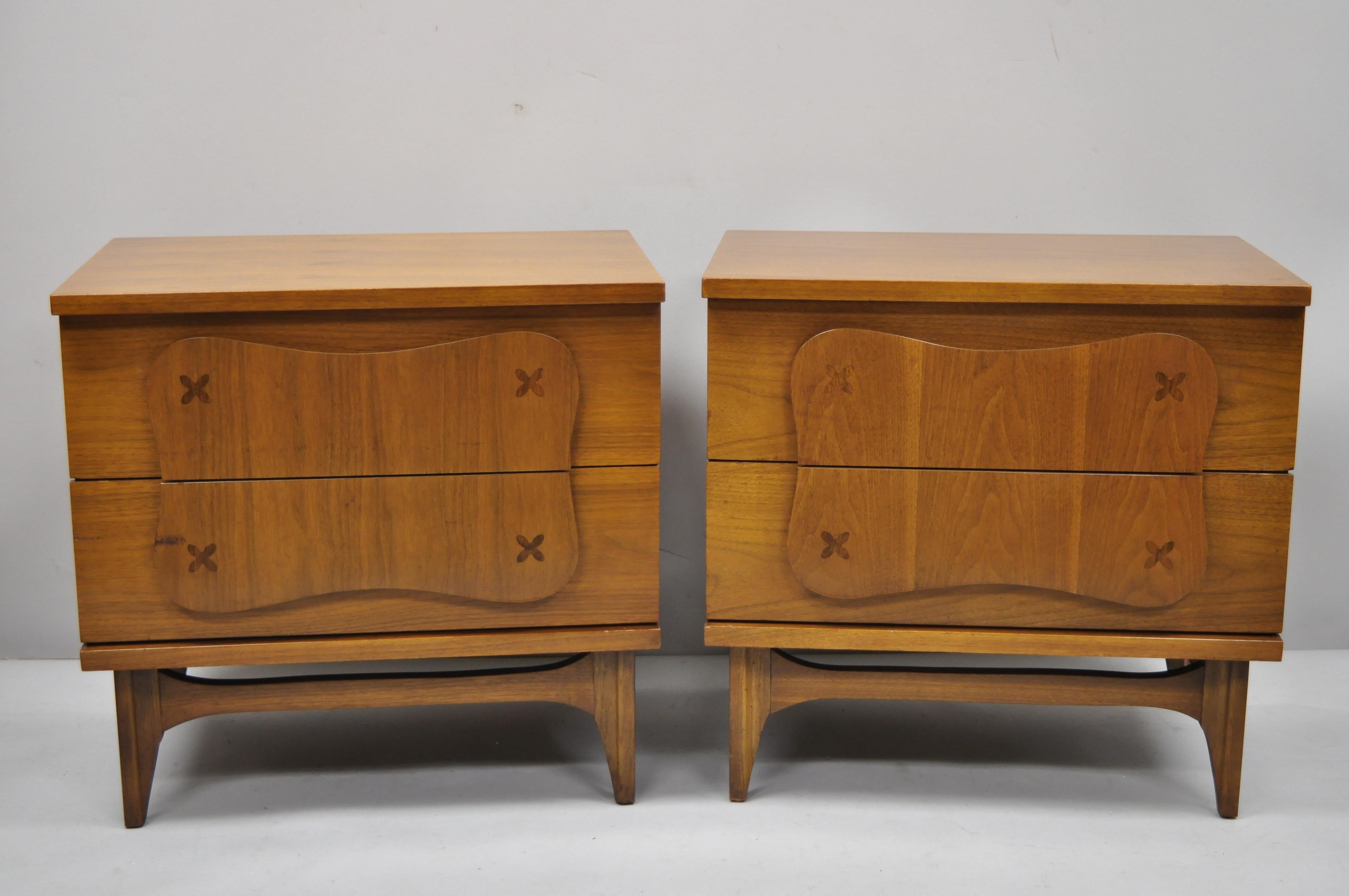 Pair of vintage Bassett Mid-Century Modern star inlay walnut nightstands bedside tables. Items feature sculpted wood pulls, star inlaid drawer fronts, tapered legs, beautiful wood grain, 2 dovetailed drawers, sleek sculptural form, circa mid-20th