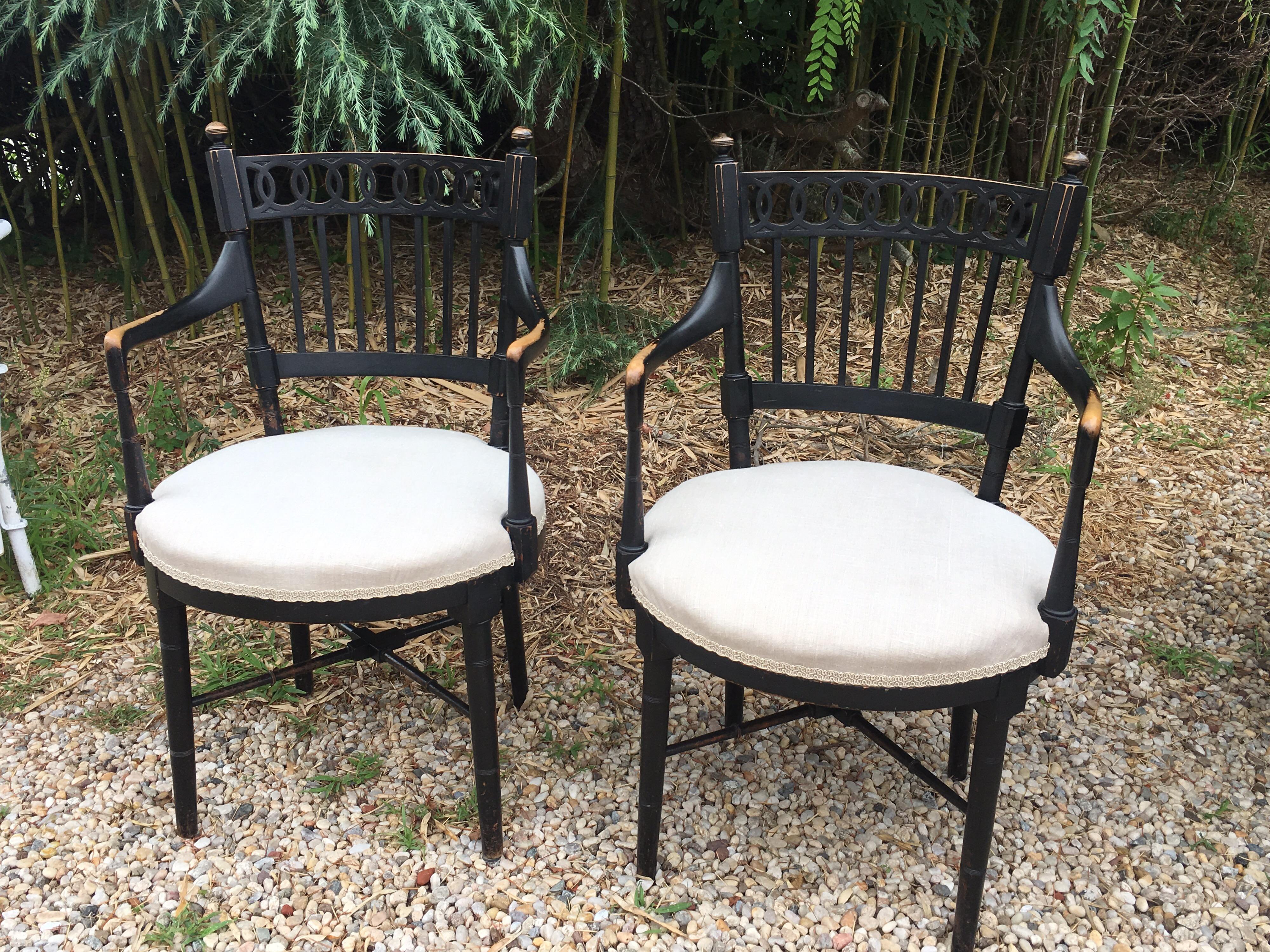 Vintage black painted armchairs, interlocking circle motif on the top rail, ball finials and upholstered in a lovely neutral linen with tape trim around.
Wear to finish, particularly at arms and legs.
