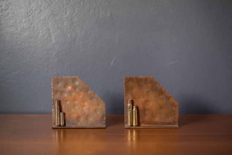 Pair of mid century trench art bookends in copper circa 1950's. Features a rustic hammered texture and bullet casing in patinated brass. The perfect accessory to organize your books or library and pairs well with industrial modern and Scandinavian