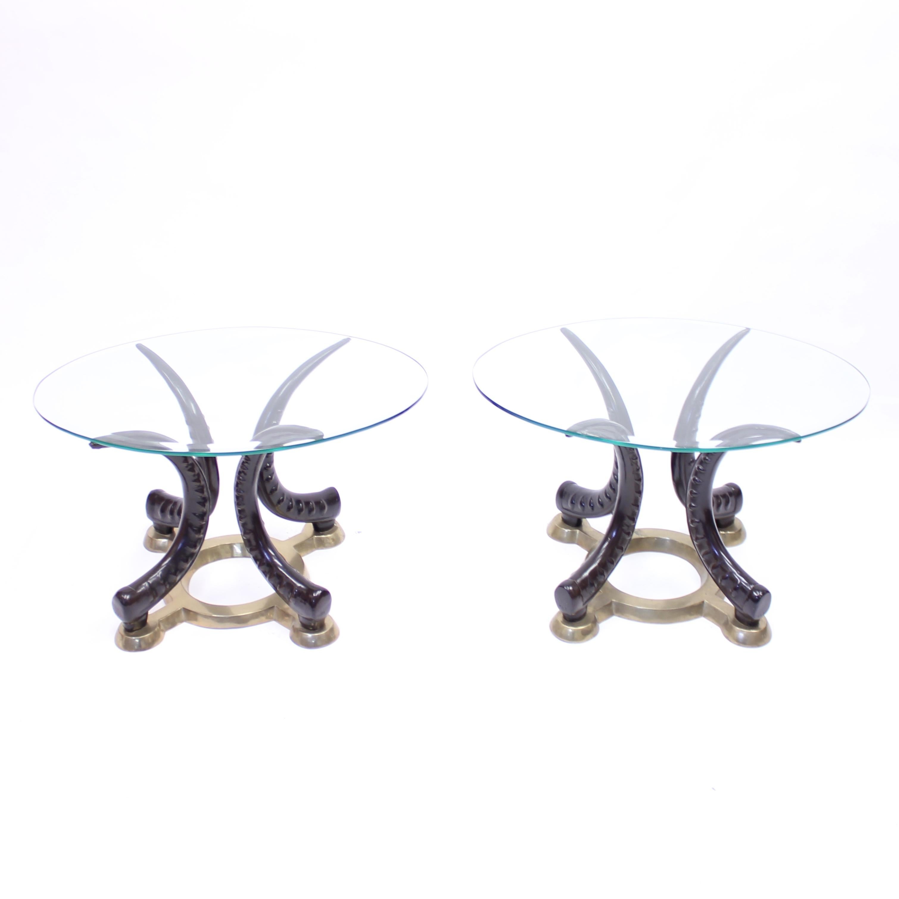 Pair of eclectic vintage brass and faux tusks side or lamp tables with oval glass tops from the 1970s or 1980s. Possibly Italian or French in origin. Round brass base with round leg holders on the outside. The faux tusk brass legs are painted to