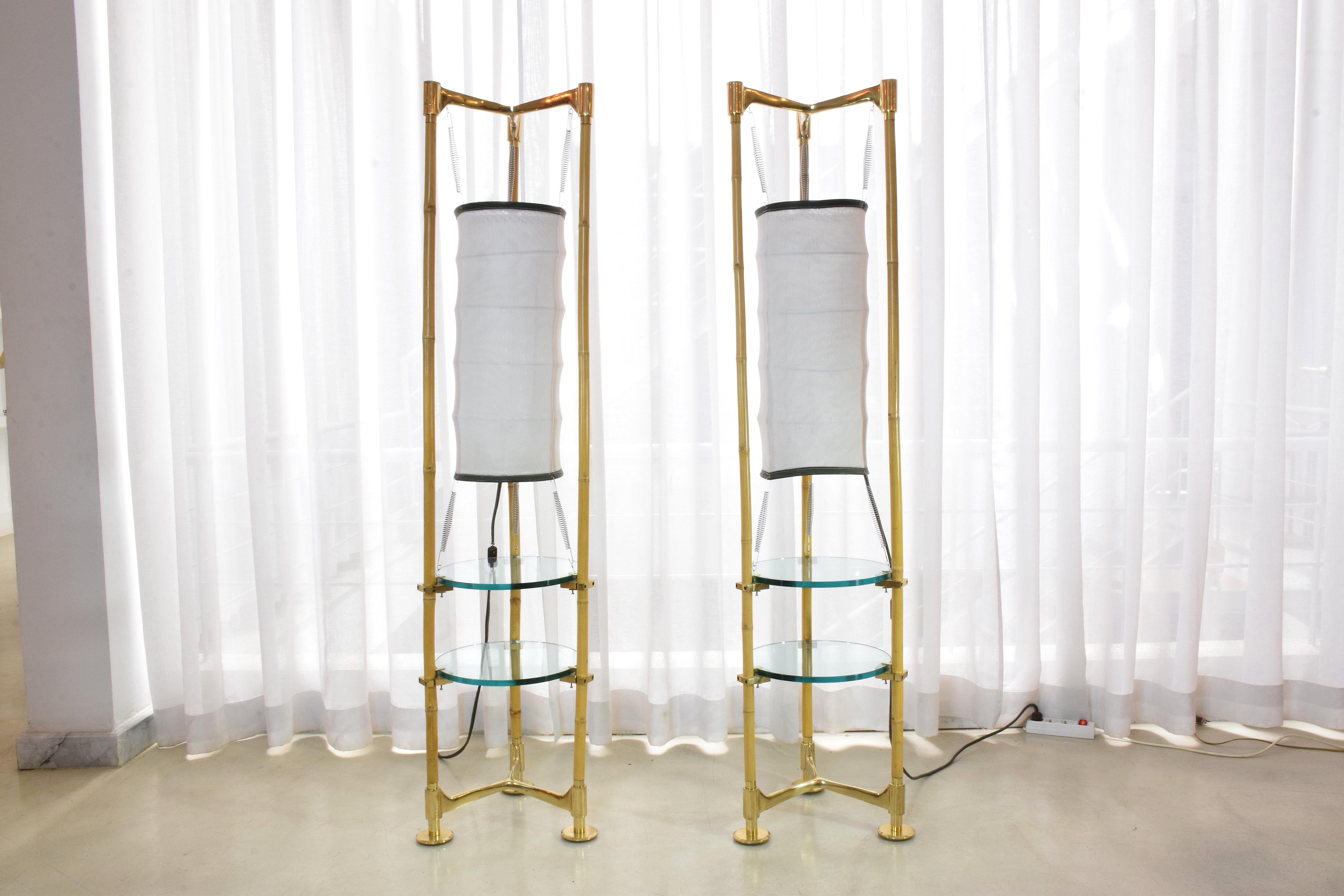 A gorgeous pair of 20th-century Italian vintage floor lamps with integrated side tables from the 1970s designed in bamboo and brass. The design is highlighted by the stylish tripod structures and Asian lantern style fabric shades with black leather